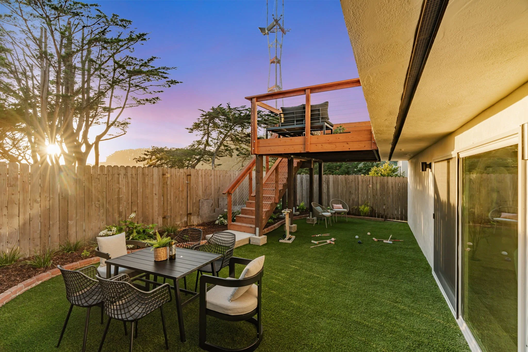 Luxury San Francisco backyard at sunset, showcasing a professional artificial turf lawn, modern outdoor dining area, and a view of the iconic Sutro Tower against a colorful sky.