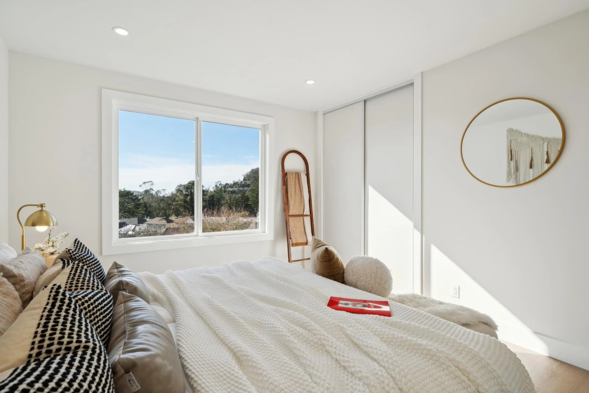 Interior view of a spacious bedroom showing a built-in closet with sliding doors, a gold circular mirror, and natural light flooding the space.