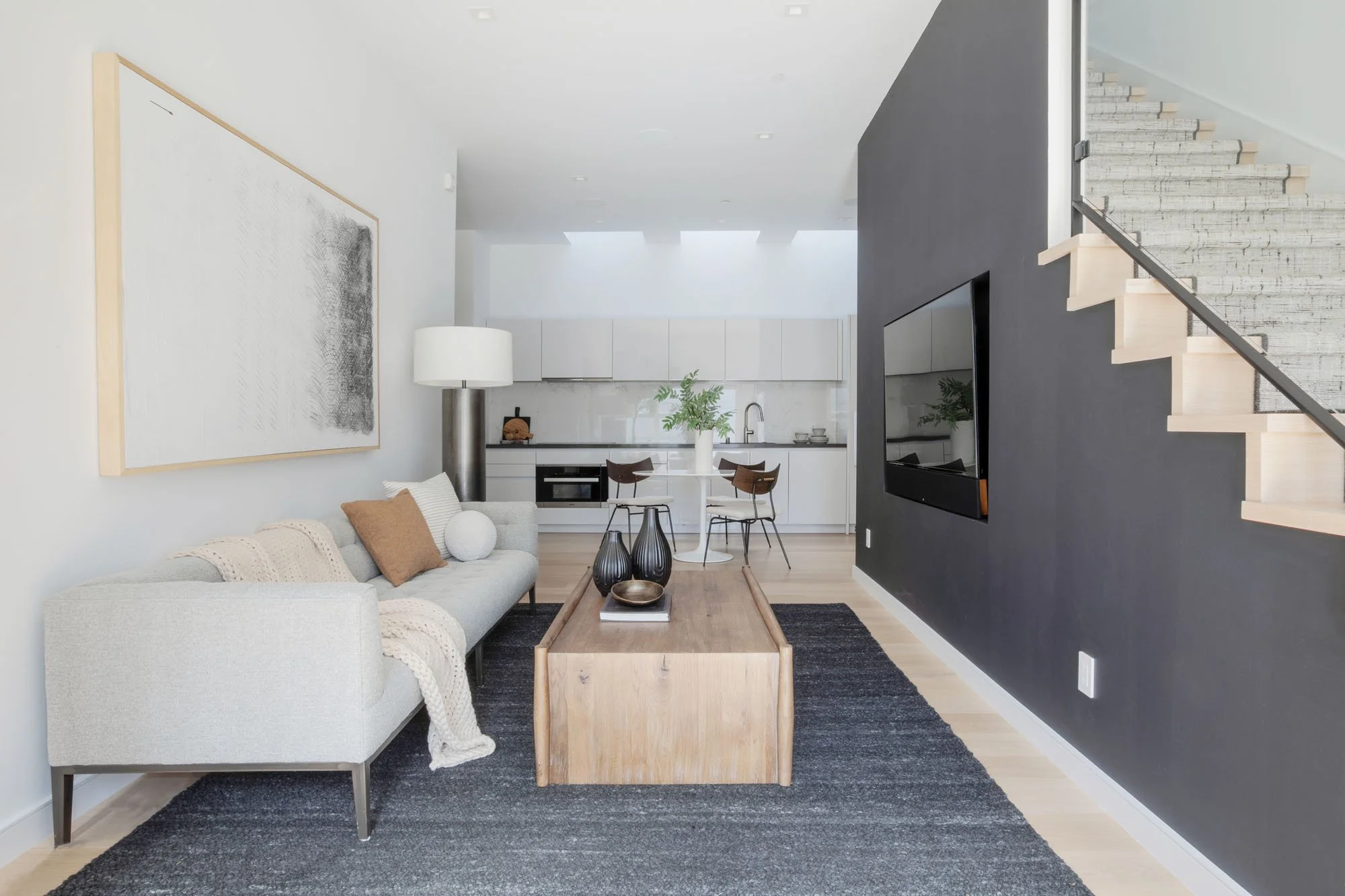 Open-concept luxury floor plan at 290 Day Street, SF, with a light gray modern sofa, abstract wall art, and views into the minimalist kitchen and dining area.