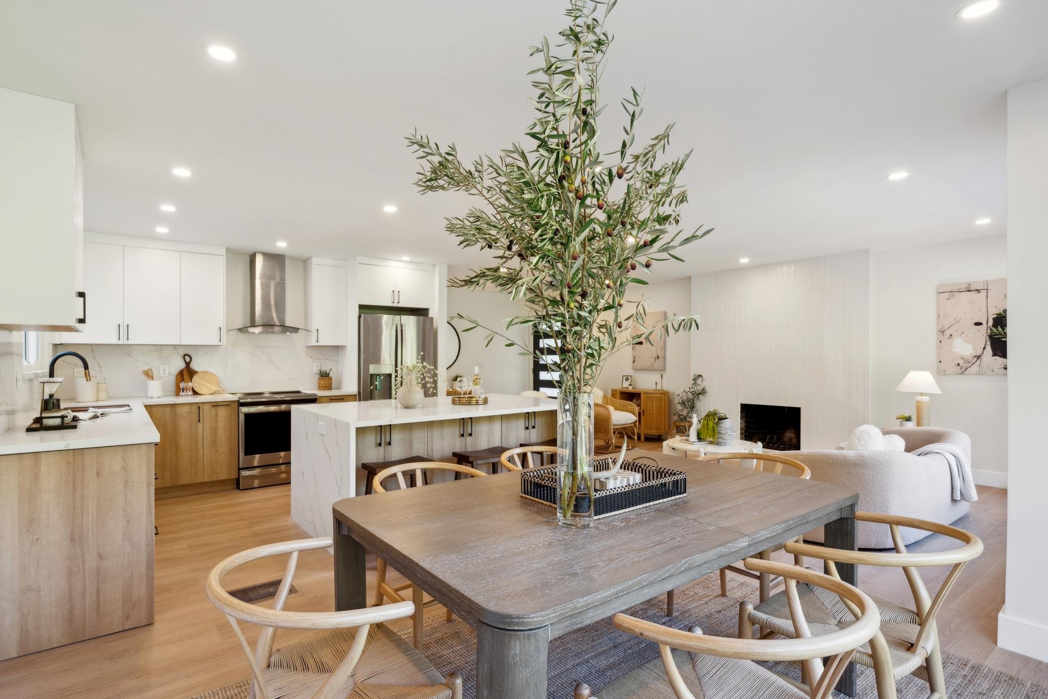 View from the dining area toward the kitchen, featuring a wood dining table, wishbone chairs, and a large kitchen island with bar seating.