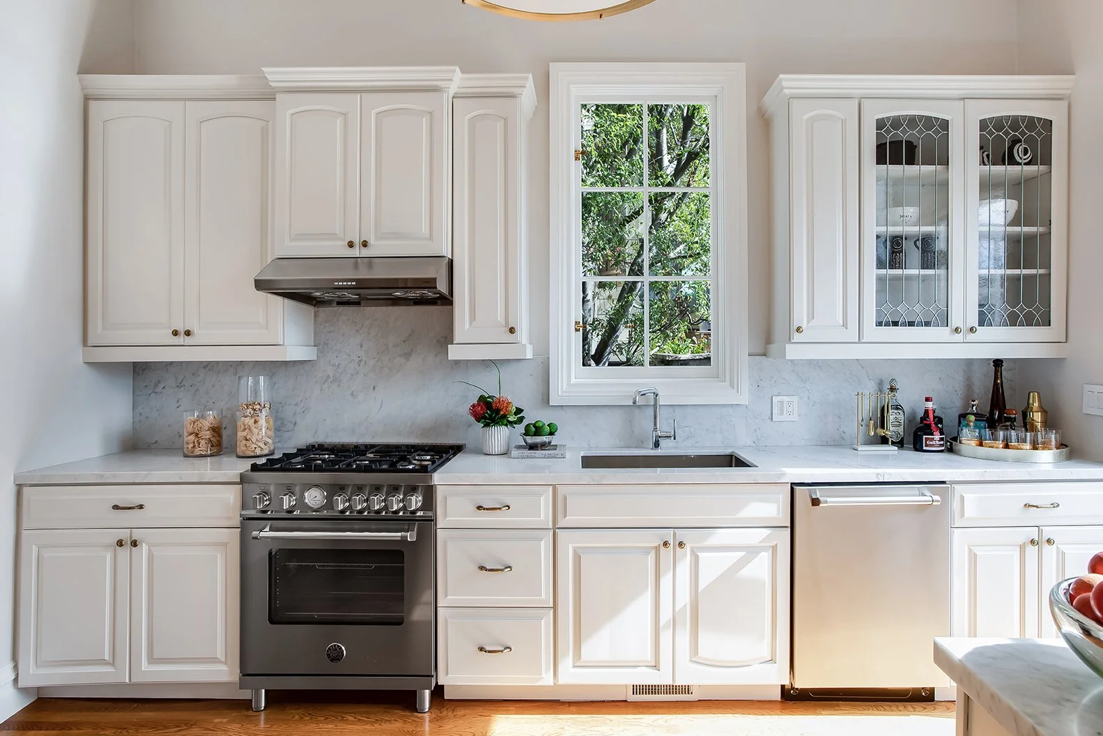 Modernized Victorian kitchen with a professional-grade gas range, marble backsplash, and a large window overlooking lush greenery.