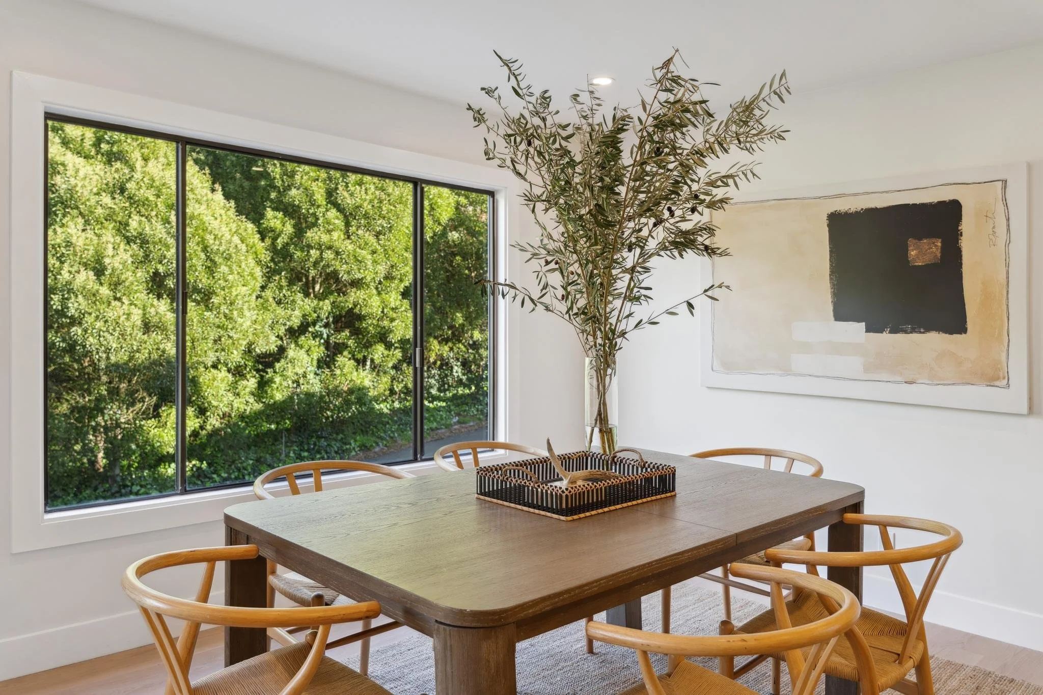 Bright dining room with a large picture window, a rustic wooden table, wishbone-style chairs, and abstract wall art in a renovated SF home.
