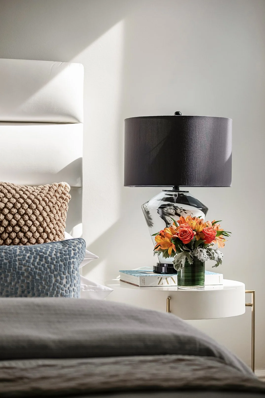 Designer bedside vignette in a luxury San Francisco bedroom featuring a modern glass lamp, professional floral staging, and a premium upholstered headboard.