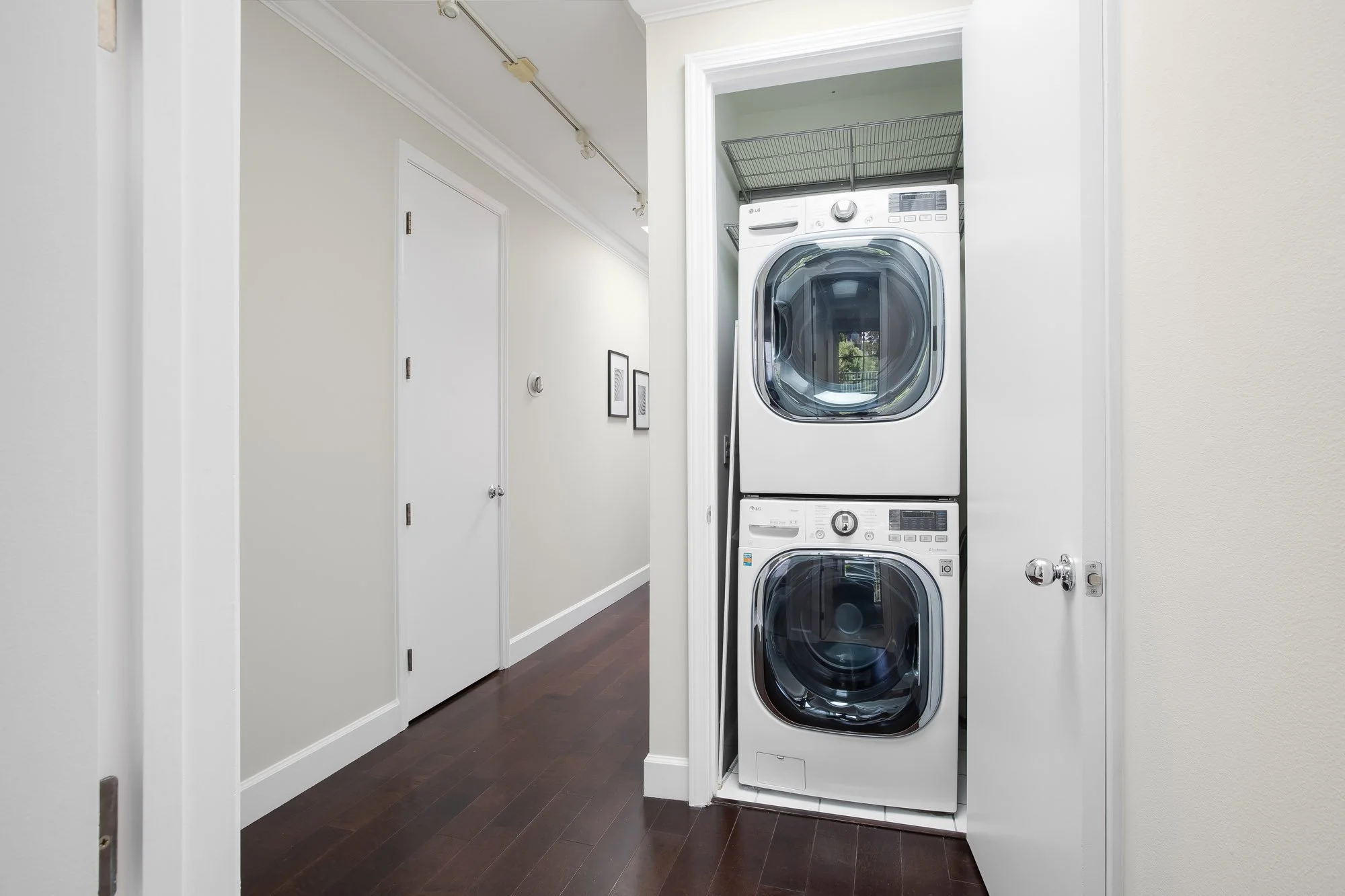 In-unit laundry at 2172 Fell Street San Francisco with stacked LG full-size washer and dryer in hallway closet, dark hardwood floors, track lighting, and multiple bedroom doors along bright corridor
