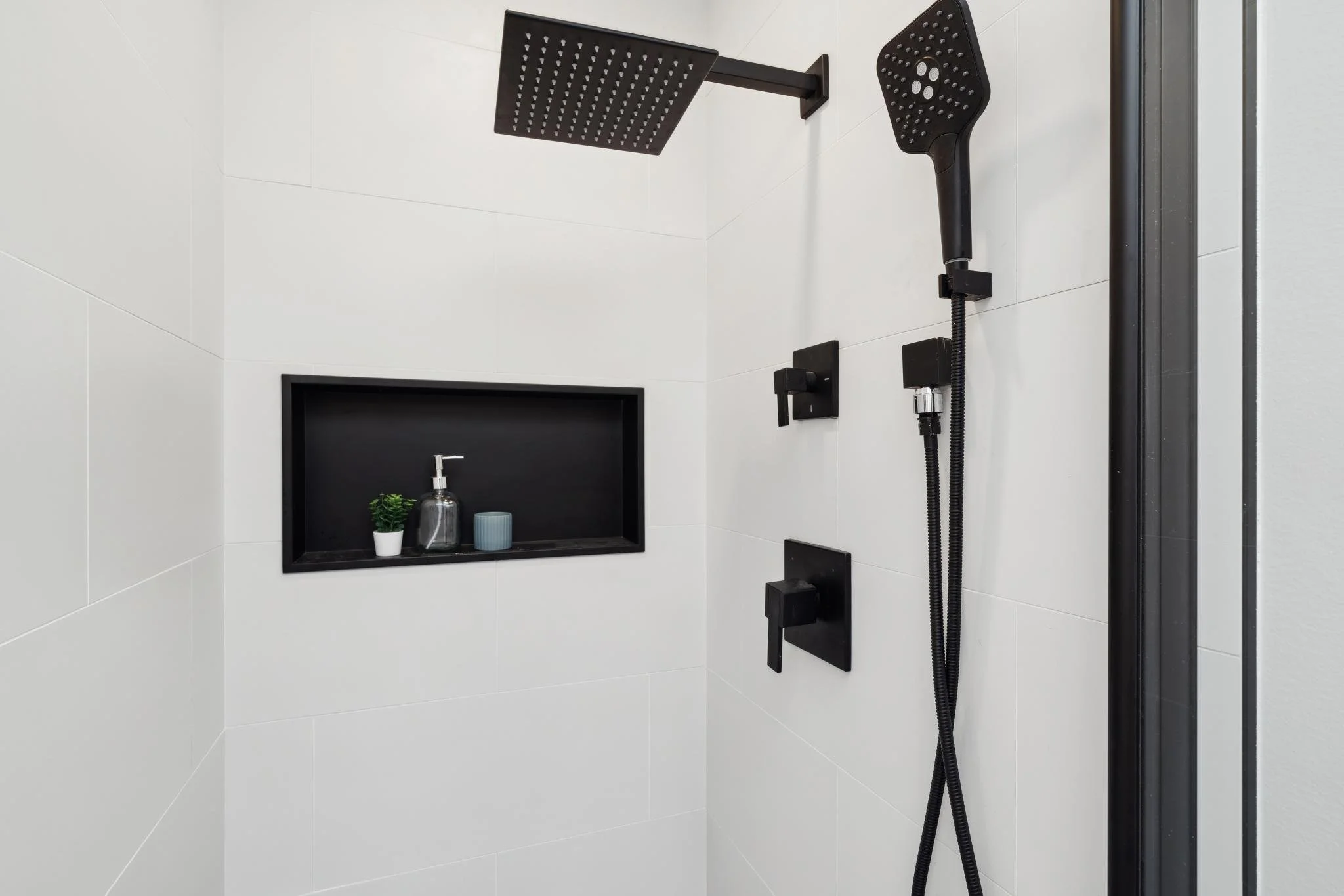 Detailed view of a luxury shower with white vertical tiles, a matte black rain showerhead, and a built-in storage niche.