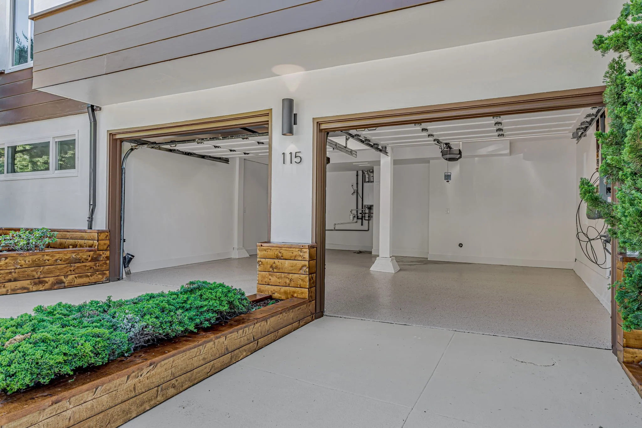 Professional two-car garage with clean white walls and gray epoxy flooring, featuring an exterior with modern lighting and tiered wooden planter boxes for curb appeal.