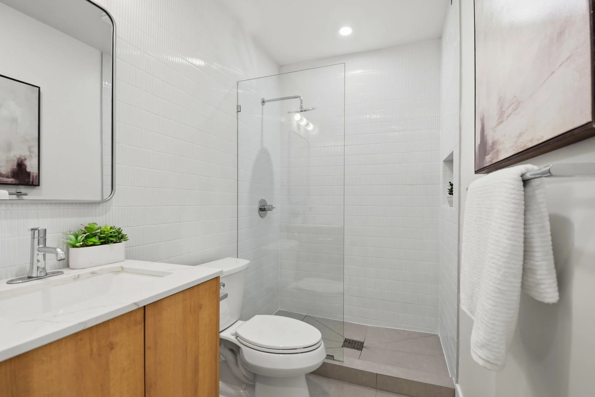 Contemporary bathroom design featuring vertical white subway tiles, a frameless glass shower, and a minimalist light oak vanity.
