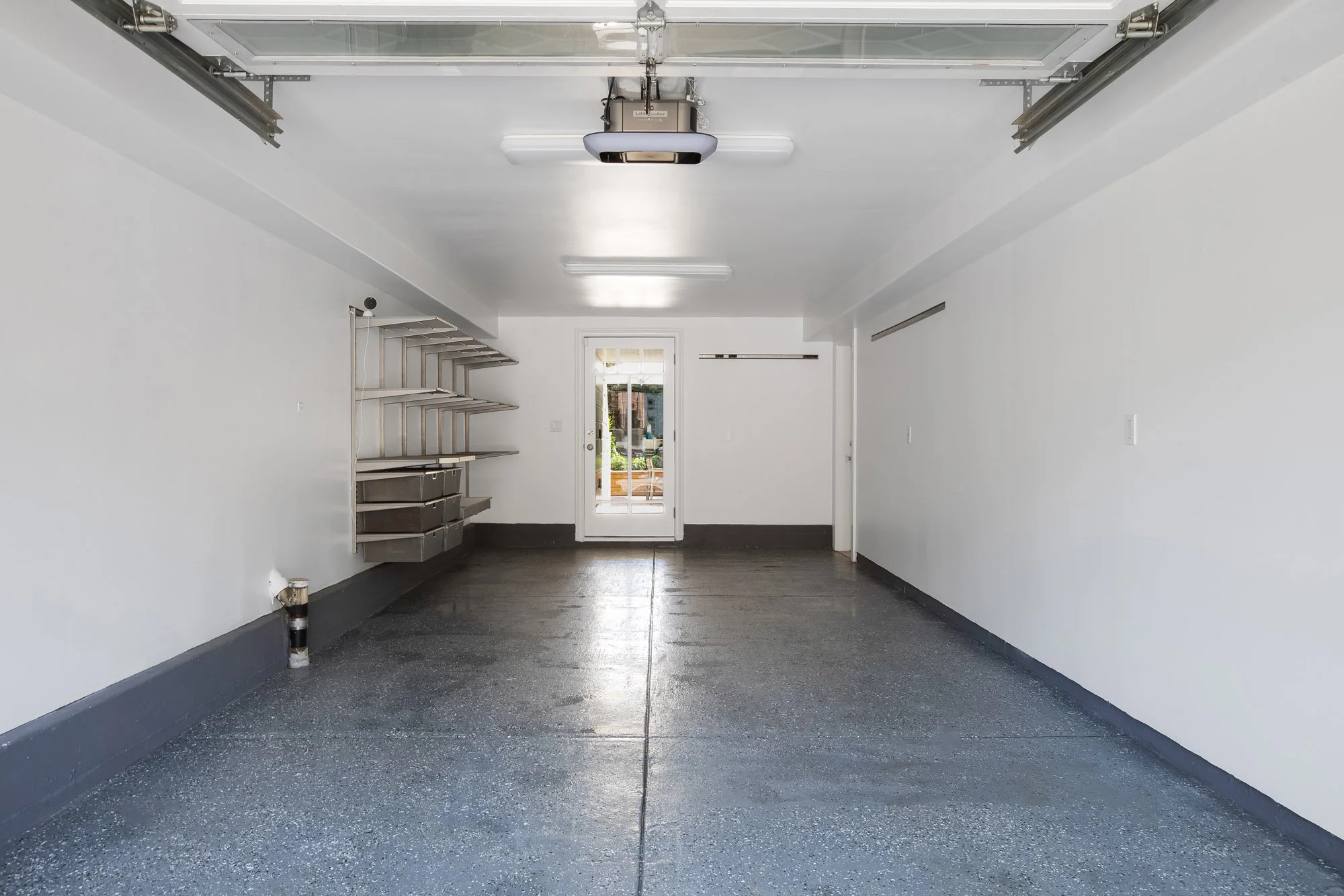 Finished one-car garage at 771 Elizabeth Street in Noe Valley with an epoxy-coated floor, built-in storage shelving, interior access, and a glass-paned door opening to the backyard.