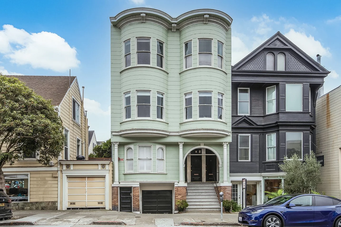 Exterior facade of three-story Victorian flat at 3517 Sacramento Street with curved bay windows, ornate cornice detailing, arched entry, and sage green painted exterior on tree-lined street in Presidio Heights, San Francisco
