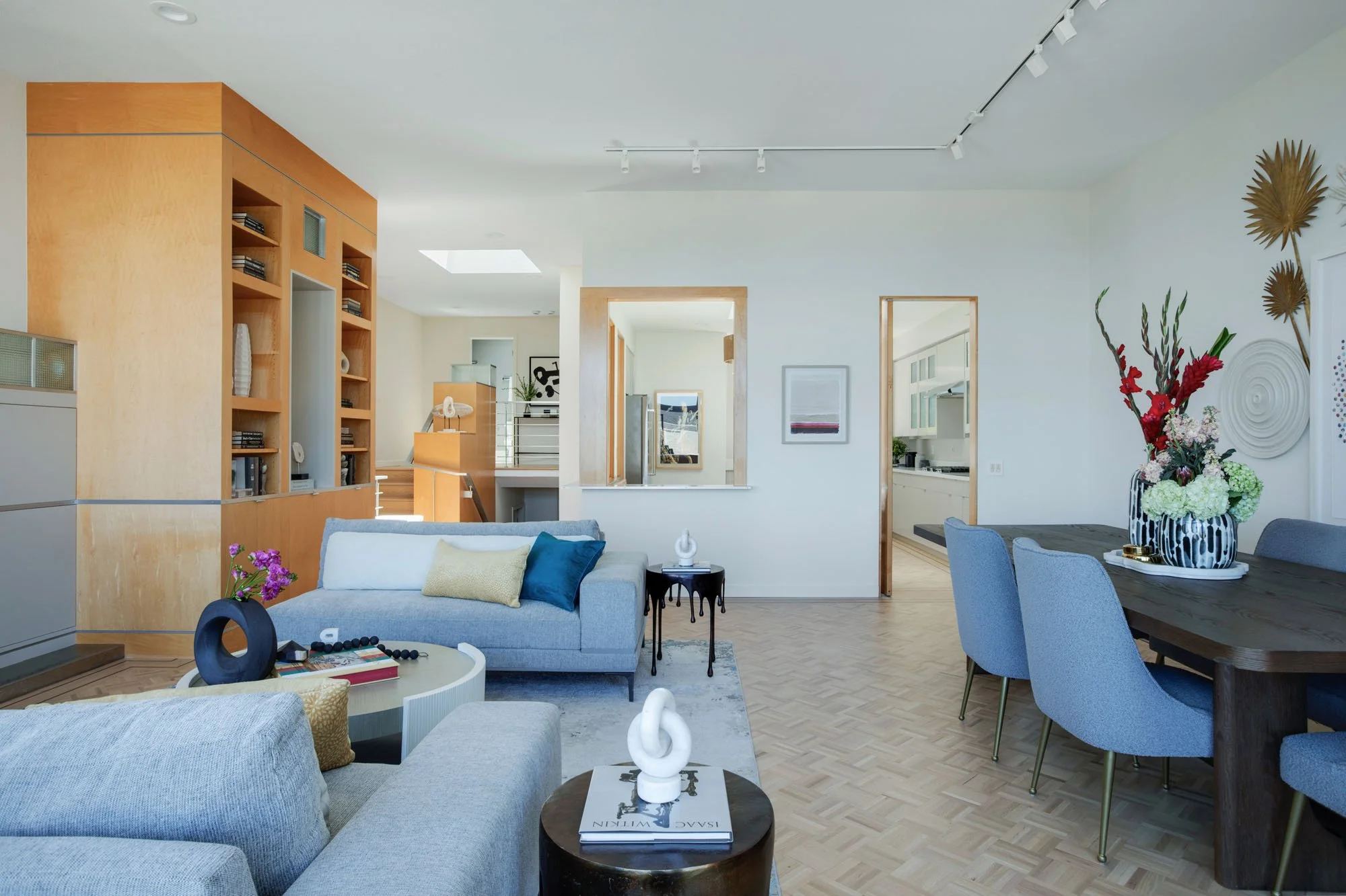 Bright open-concept living and dining area with designer furniture, custom wood built-in cabinetry, and parquet hardwood floors with elegant dark wood inlays.