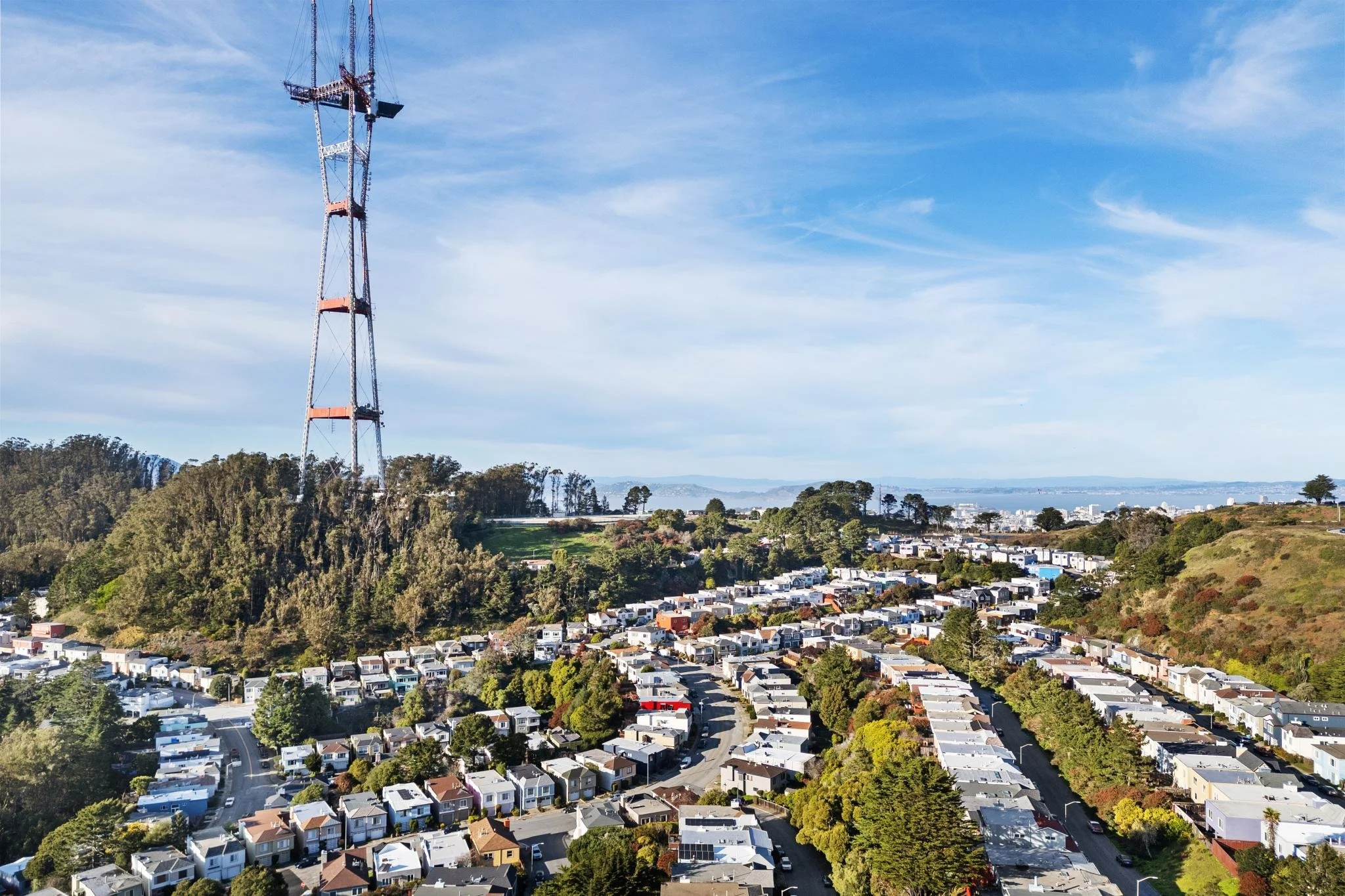 Panoramic drone shot of San Francisco's hillside homes with Sutro Tower as a landmark and a distant view of the San Francisco Bay.