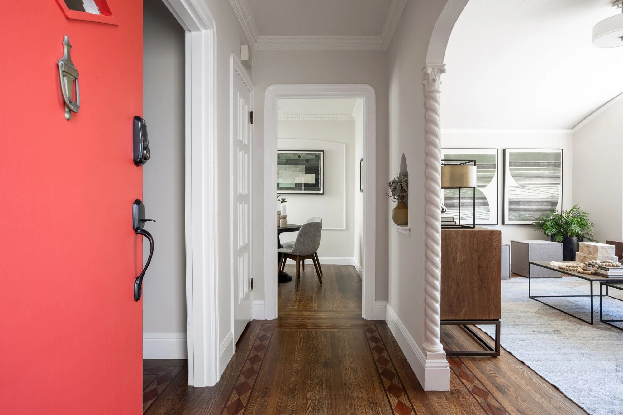 View from the red entry door showing the hallway’s intricate walnut floor inlays and transition into a modern dining space.