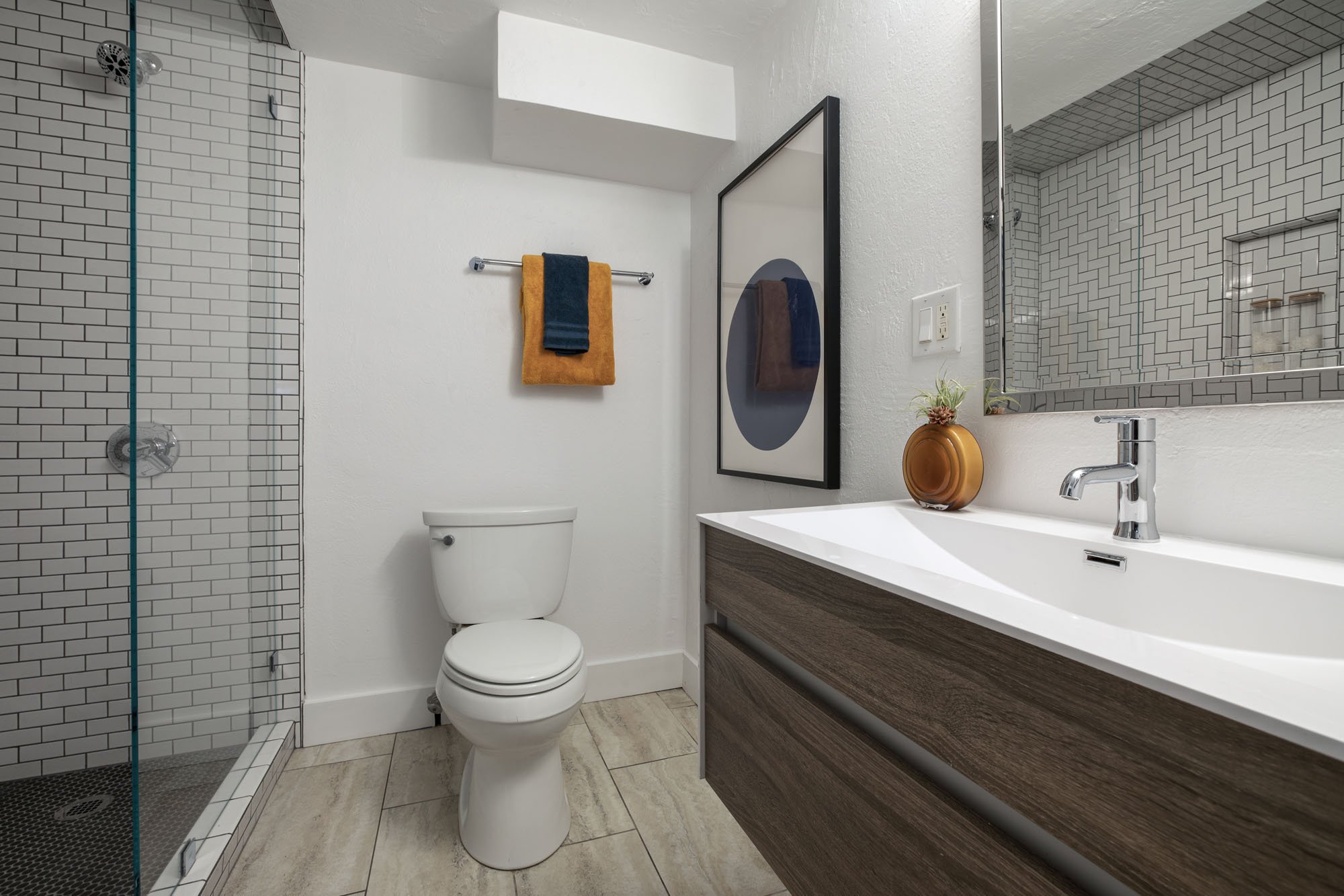 Newly renovated modern bathroom featuring a walk-in glass shower with subway tile, a floating wood vanity, and contemporary fixtures.