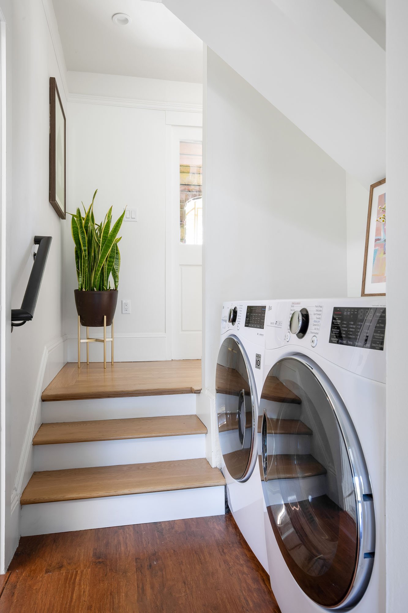 A clean and organized laundry area tucked under a staircase, featuring a side-by-side high-efficiency front-loading washer and dryer .