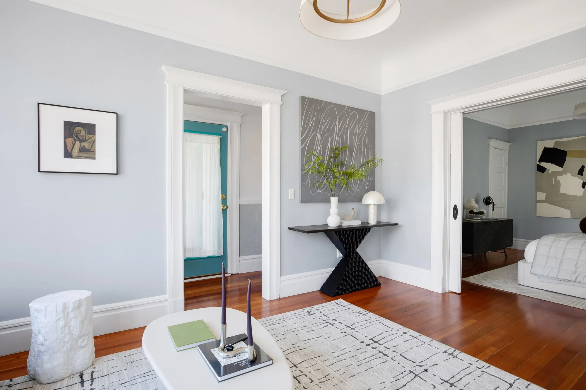 Hallway with console table and artwork, pocket door open to a bedroom, turquoise front door visible beyond