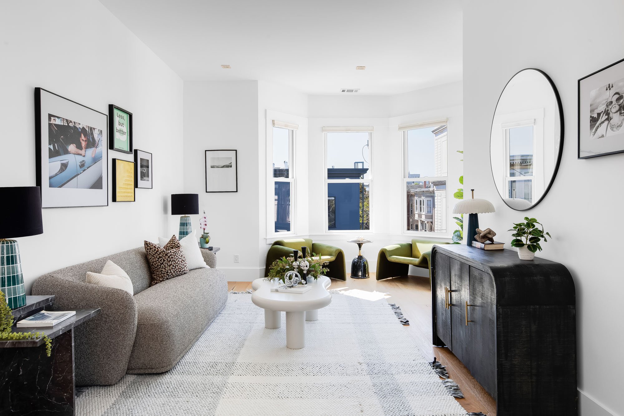 Luxury living room with a grey textured sofa, gallery wall, and green velvet accent chairs set in a classic San Francisco bay window.
