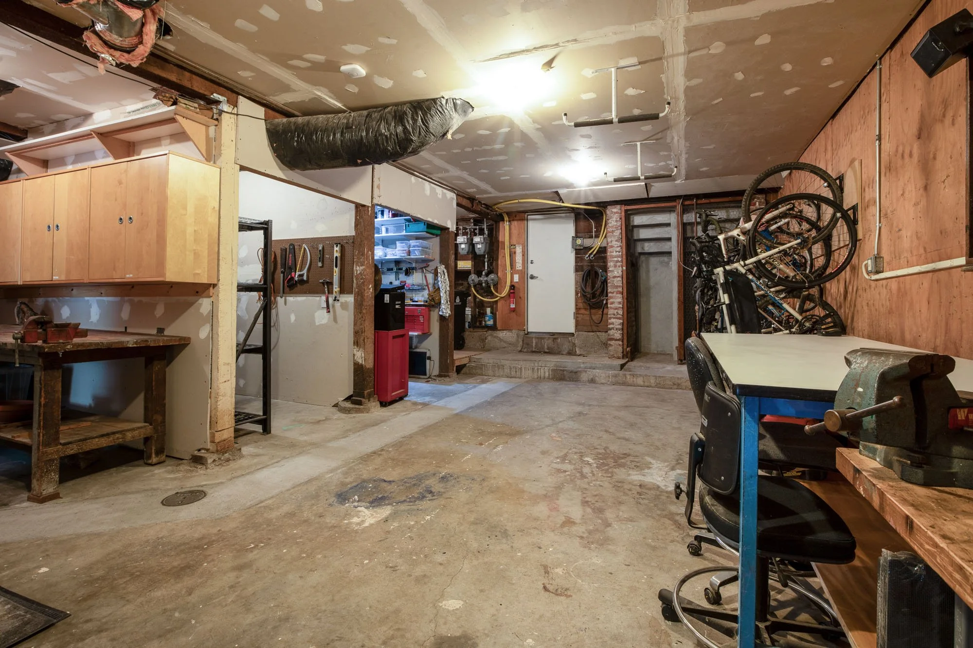 Large unfinished basement workshop with a heavy-duty wood workbench, wall-mounted tool storage, and ample space for bike storage and DIY projects.