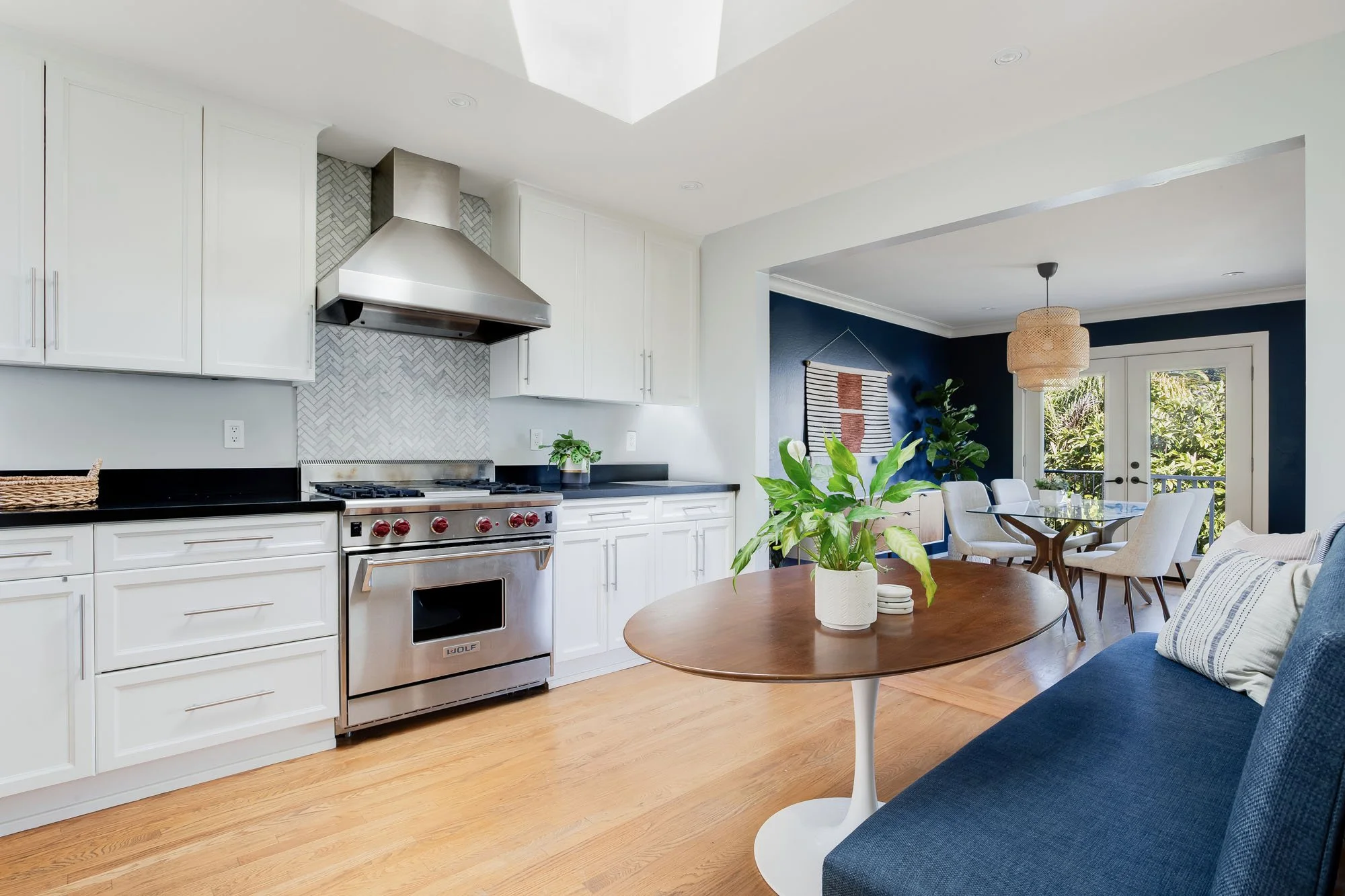Modern kitchen detail showing a professional-grade Wolf stainless steel gas range, herringbone tile backsplash, and black stone countertops.