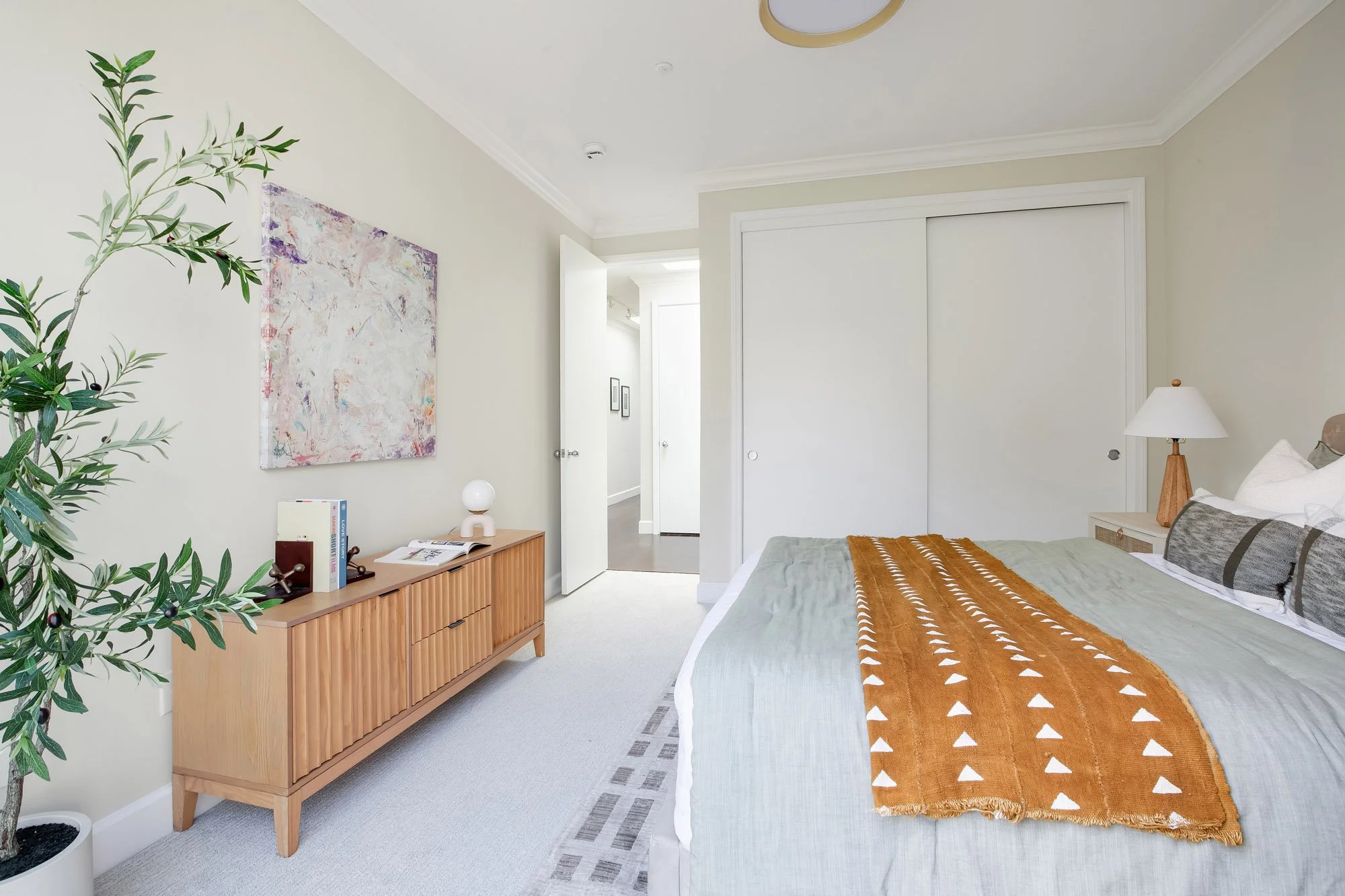 Secondary bedroom at 2172 Fell Street San Francisco showing built-in closet, fluted oak dresser, abstract canvas wall art, new carpet flooring, and open door to lit hallway with crown molding throughout