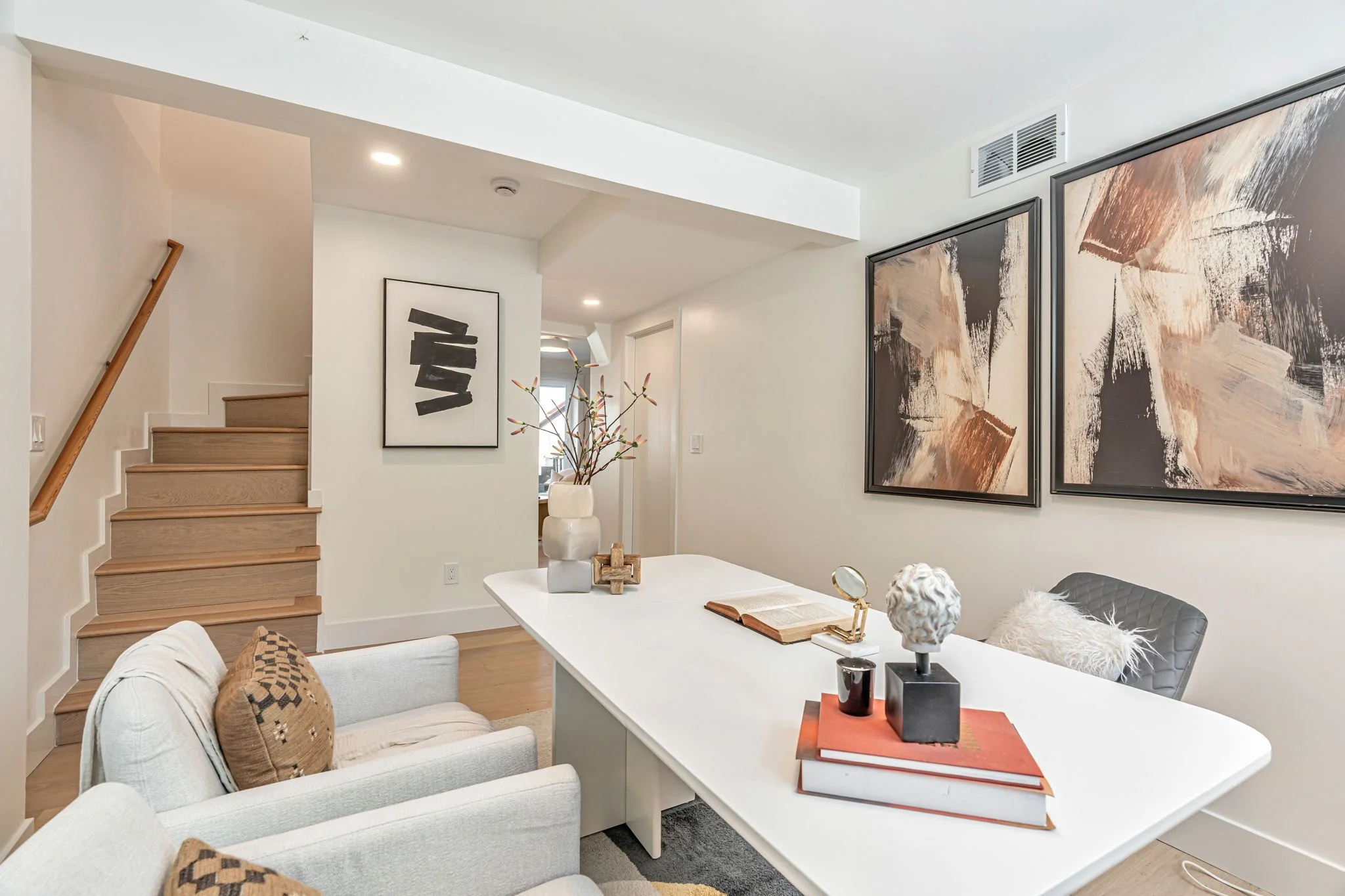 Contemporary home office interior with a wood-tread staircase, light oak floors, and large-scale framed abstract paintings for a sophisticated aesthetic.