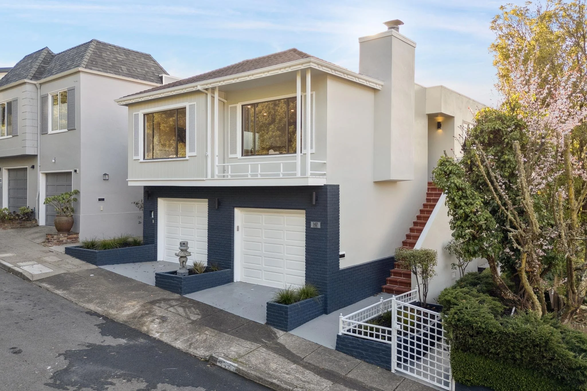Side-angle view of 147 Gladeview Way, a modern SF residence showing the white stucco exterior, a prominent chimney, and a terracotta-tiled staircase leading to the main entrance.