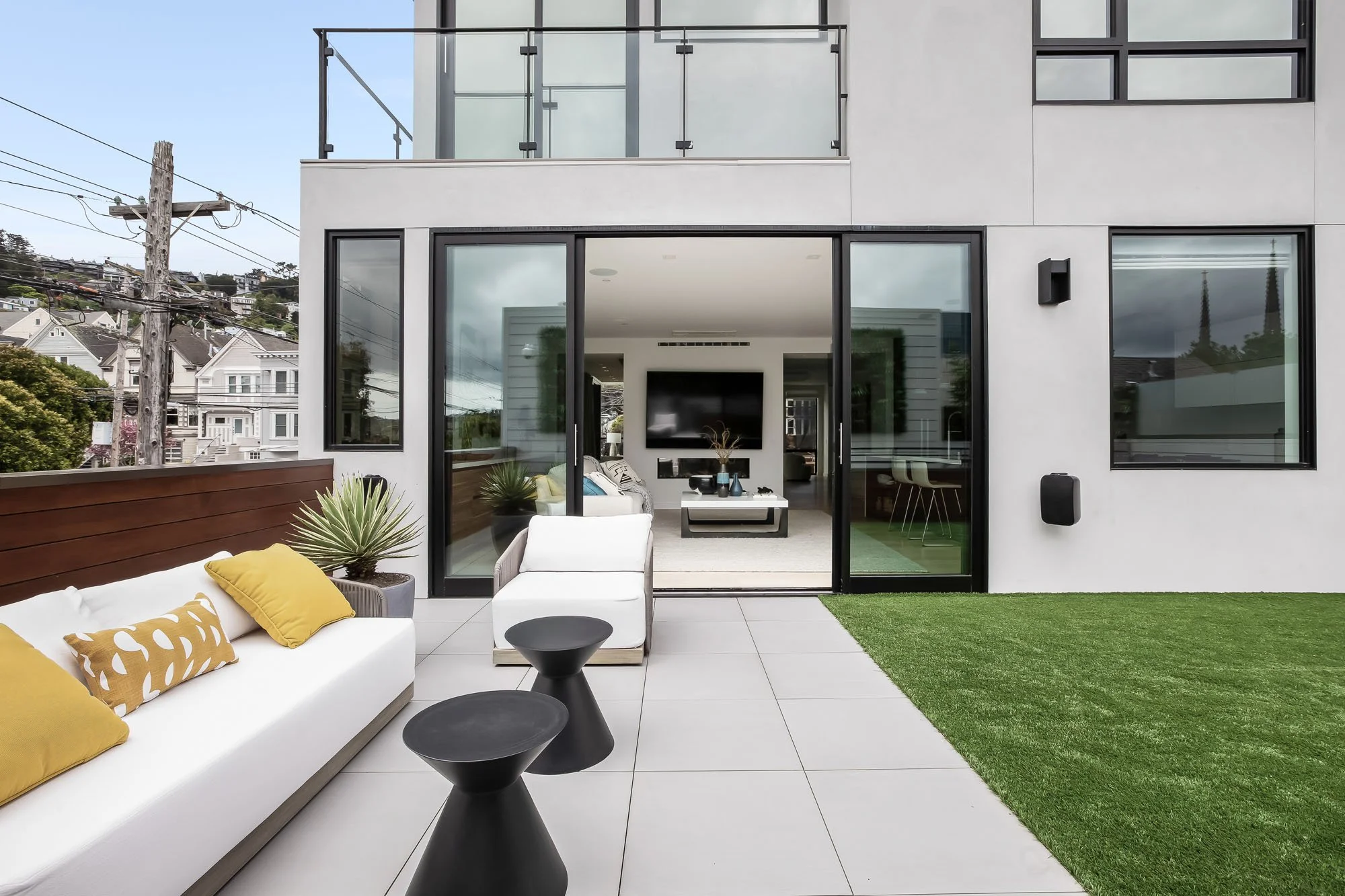 Designer backyard patio at 1647 Sanchez featuring modern white outdoor furniture, artificial turf, and views of San Francisco’s iconic Victorian architecture.