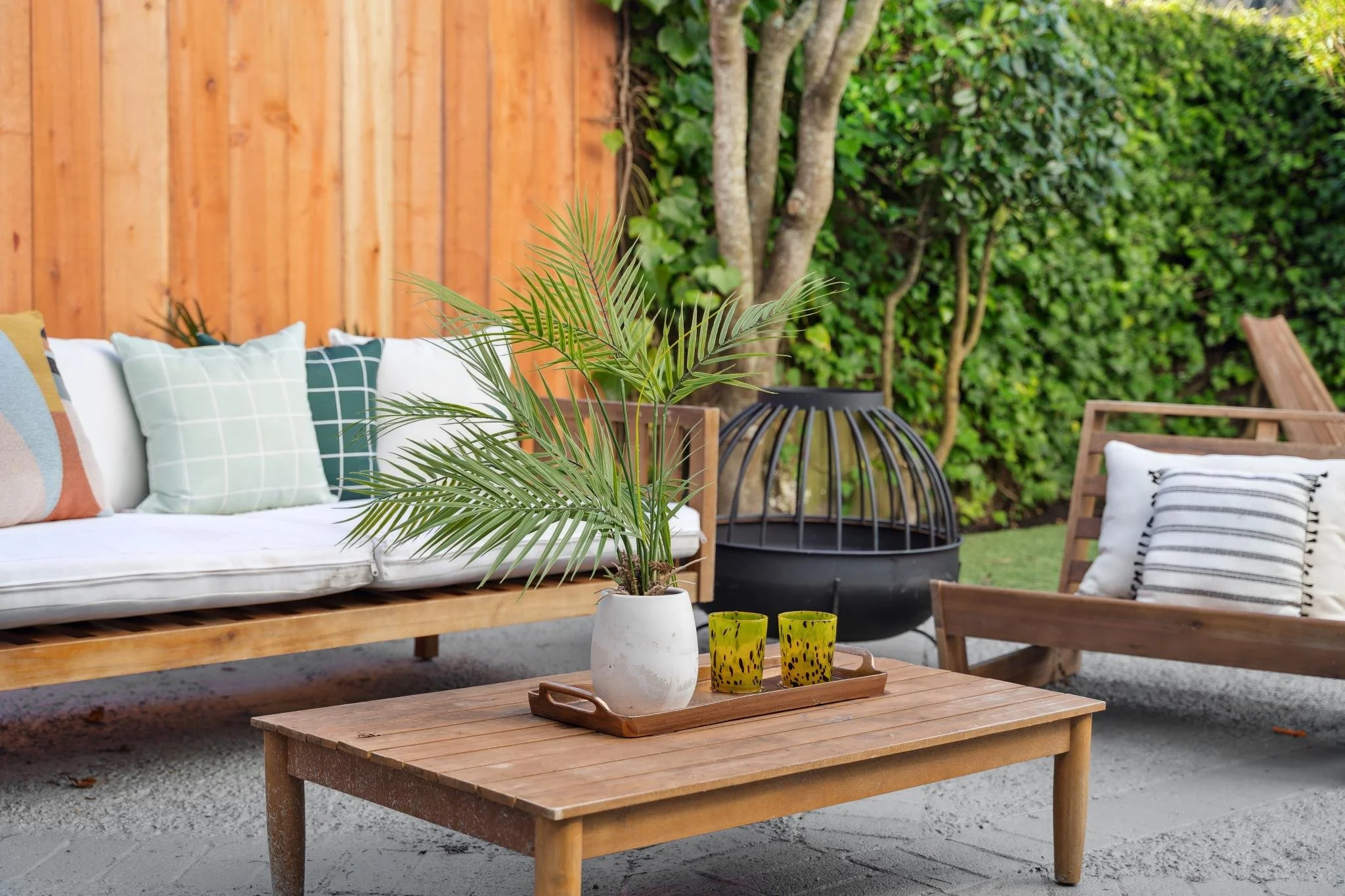 Close-up of a modern outdoor seating area featuring a wooden coffee table with a potted palm, perfect for entertaining in a San Francisco garden.