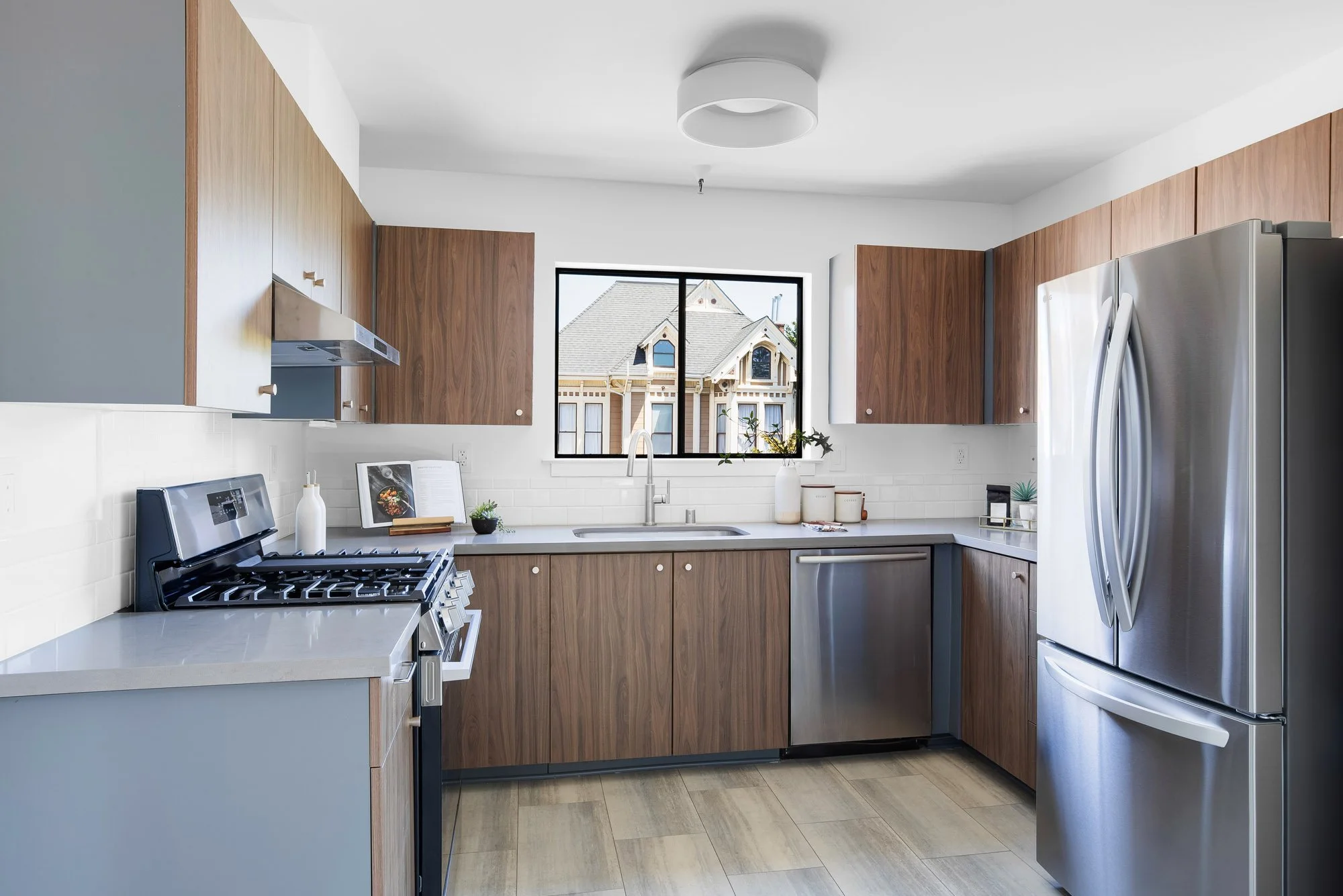Renovated kitchen at 932 Broderick Street #2 with walnut cabinetry, quartz countertops, stainless steel appliances, gas range, and a window framing a San Francisco Victorian.