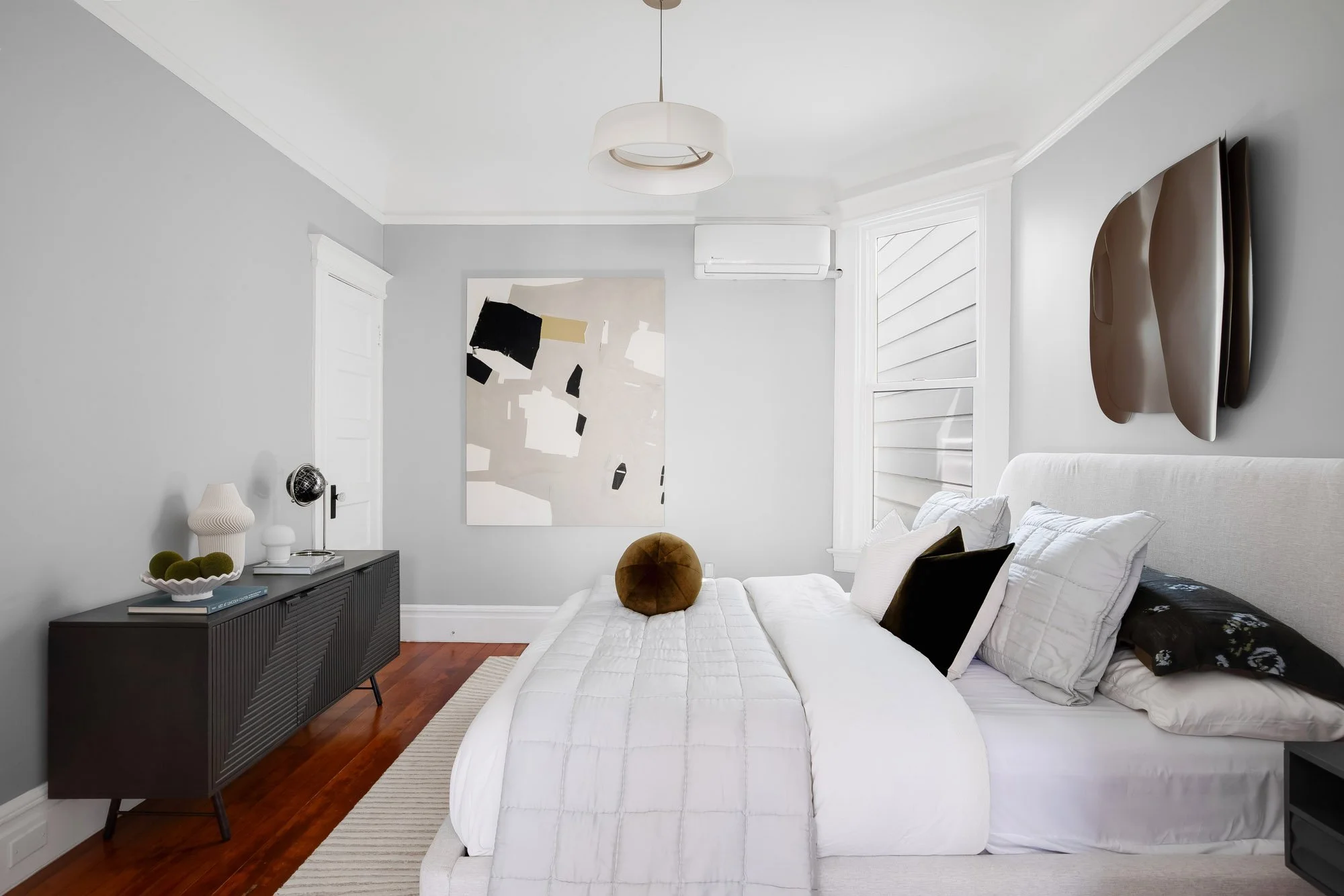 Bedroom with wall-mounted mini-split, abstract wall art, and a dark wood dresser