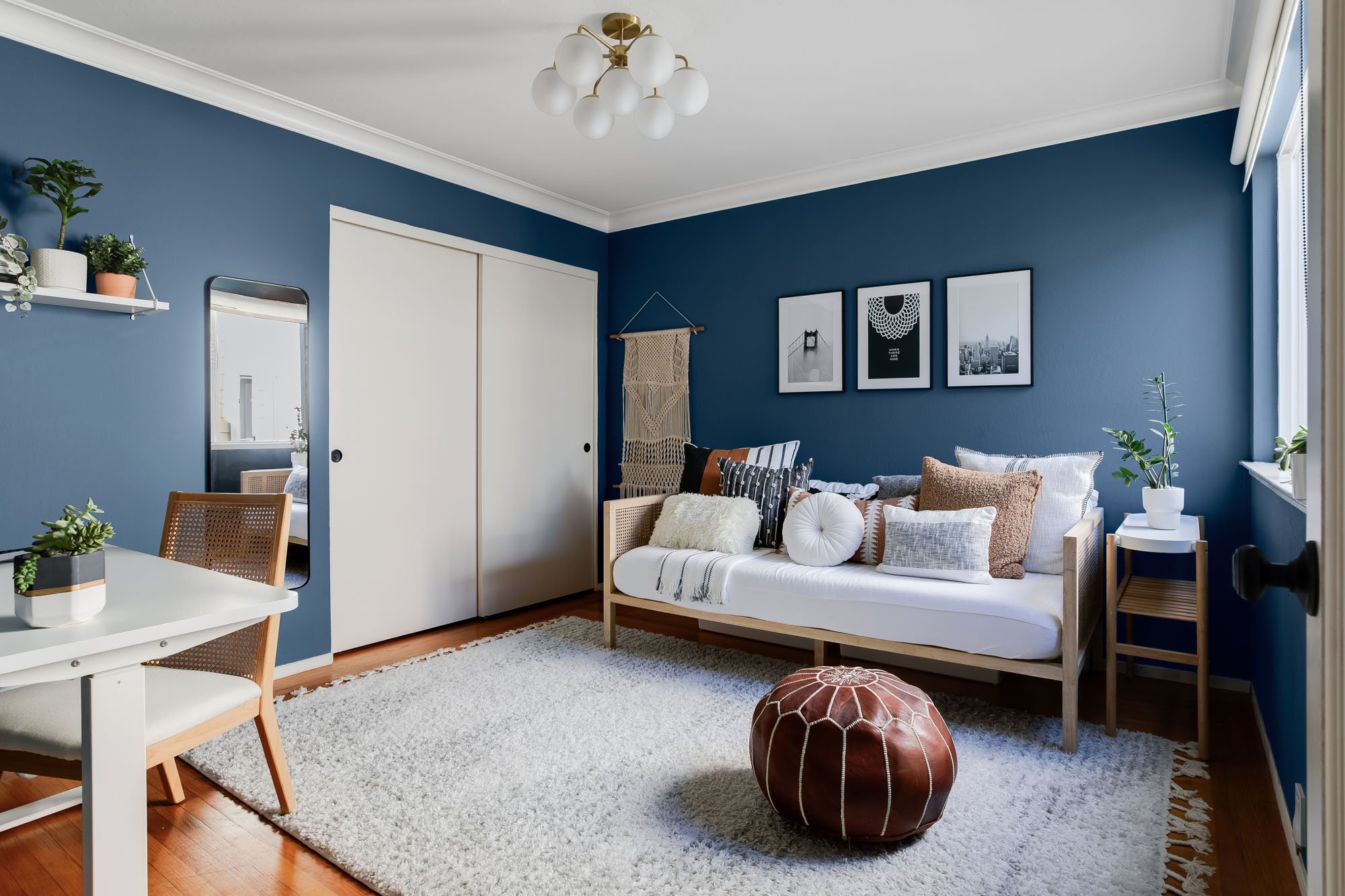 Cozy bedroom or home office with blue walls, a white daybed with textured pillows, and a leather Moroccan pouf on a shag rug.