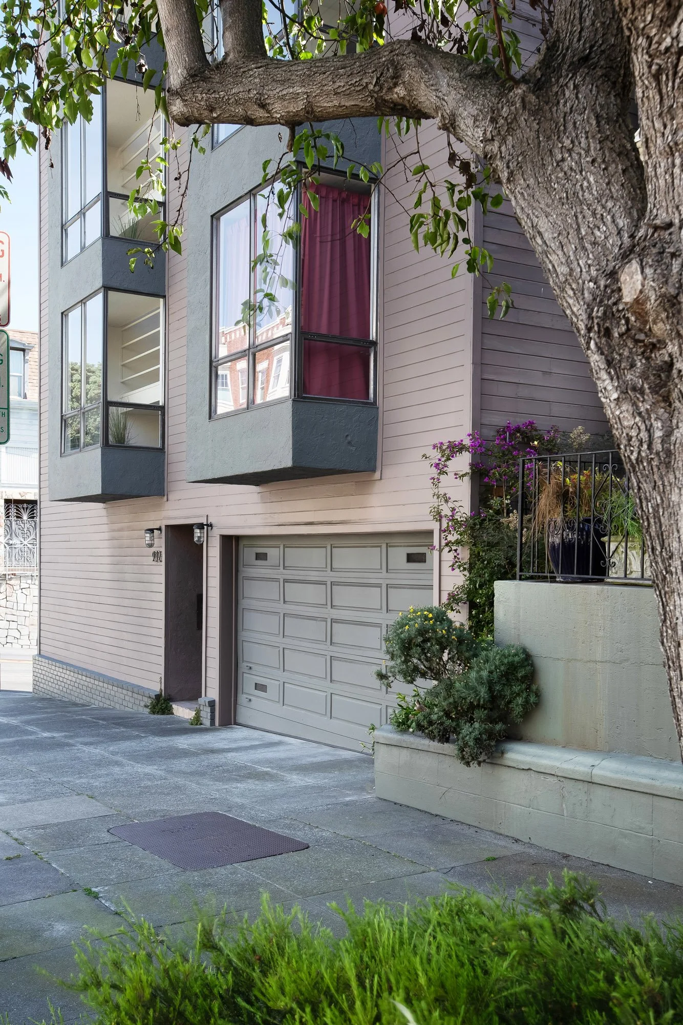 Ground-level entry and one-car garage of 932 Broderick Street #2 framed by a mature street tree and flowering bougainvillea.