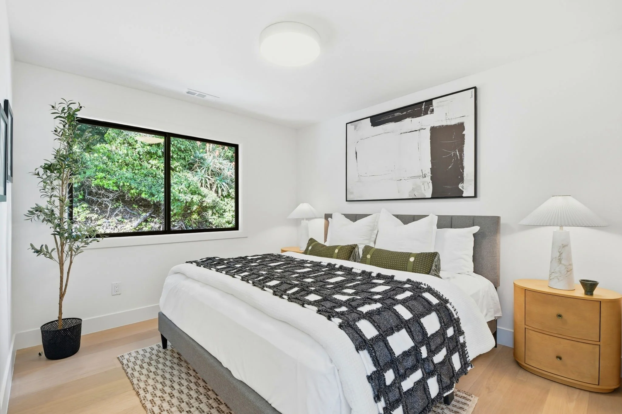 Primary bedroom suite in Midtown Terrace, San Francisco, featuring a grey upholstered bed, abstract art, and a large picture window overlooking lush hillside greenery.