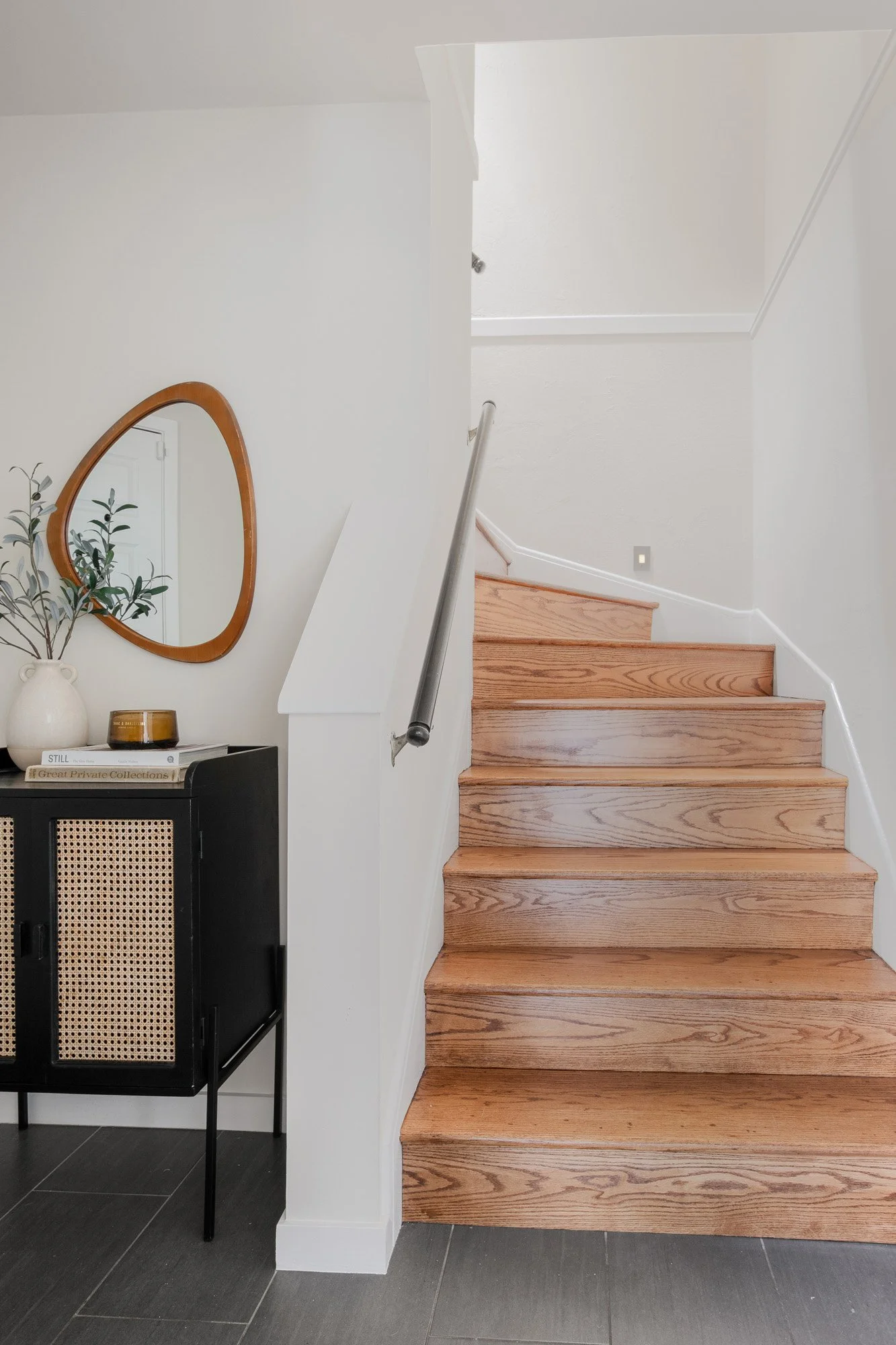 Elegant interior entryway featuring a natural wood staircase, slate tile flooring, and a black cane-front storage cabinet.
