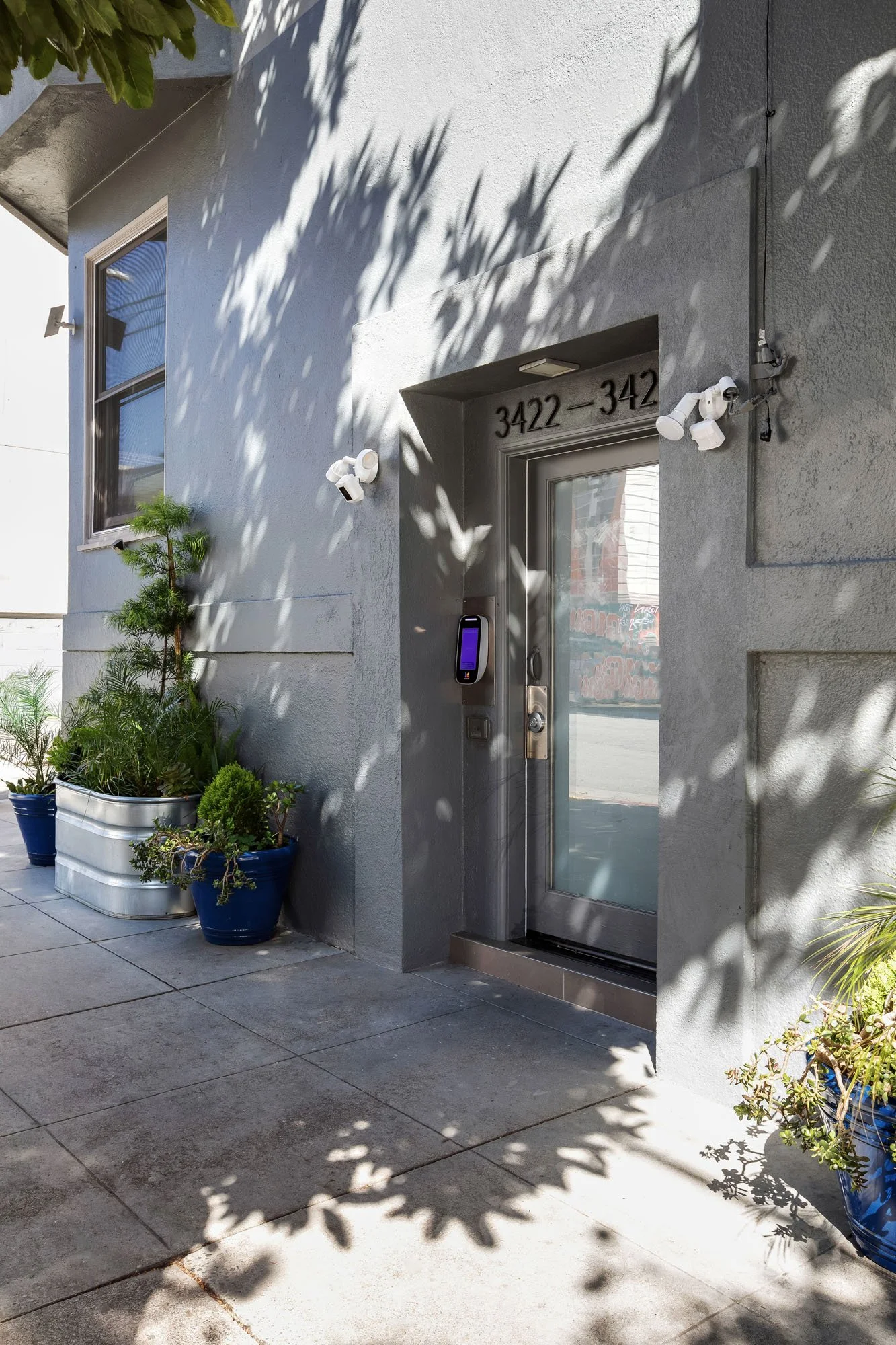 Secure modern entrance to 3422-3428 19th St featuring keyless smart entry, security cameras, and decorative blue potted plants.