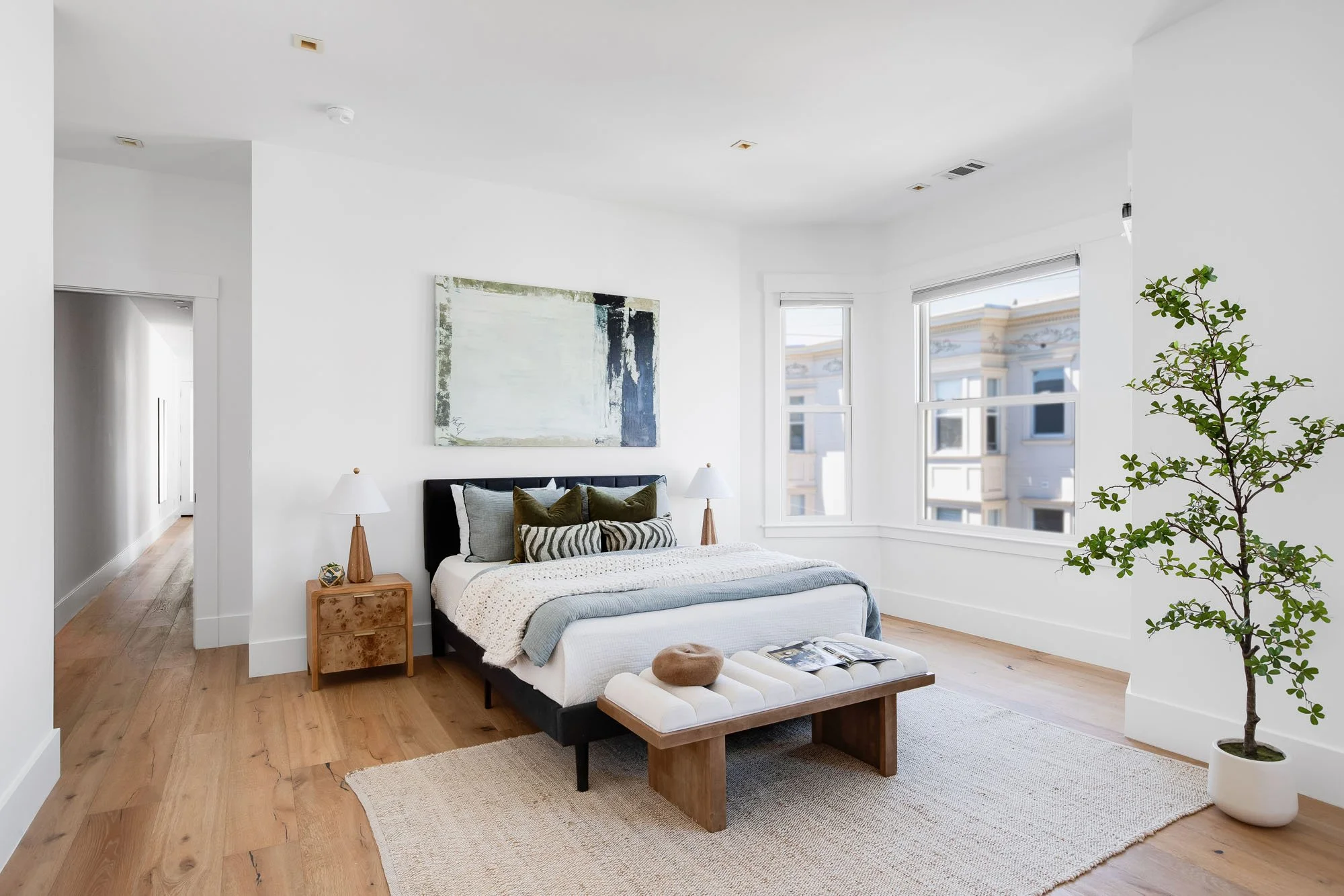 Designer primary bedroom featuring a king-size bed, large abstract painting, and natural light from San Francisco bay windows.