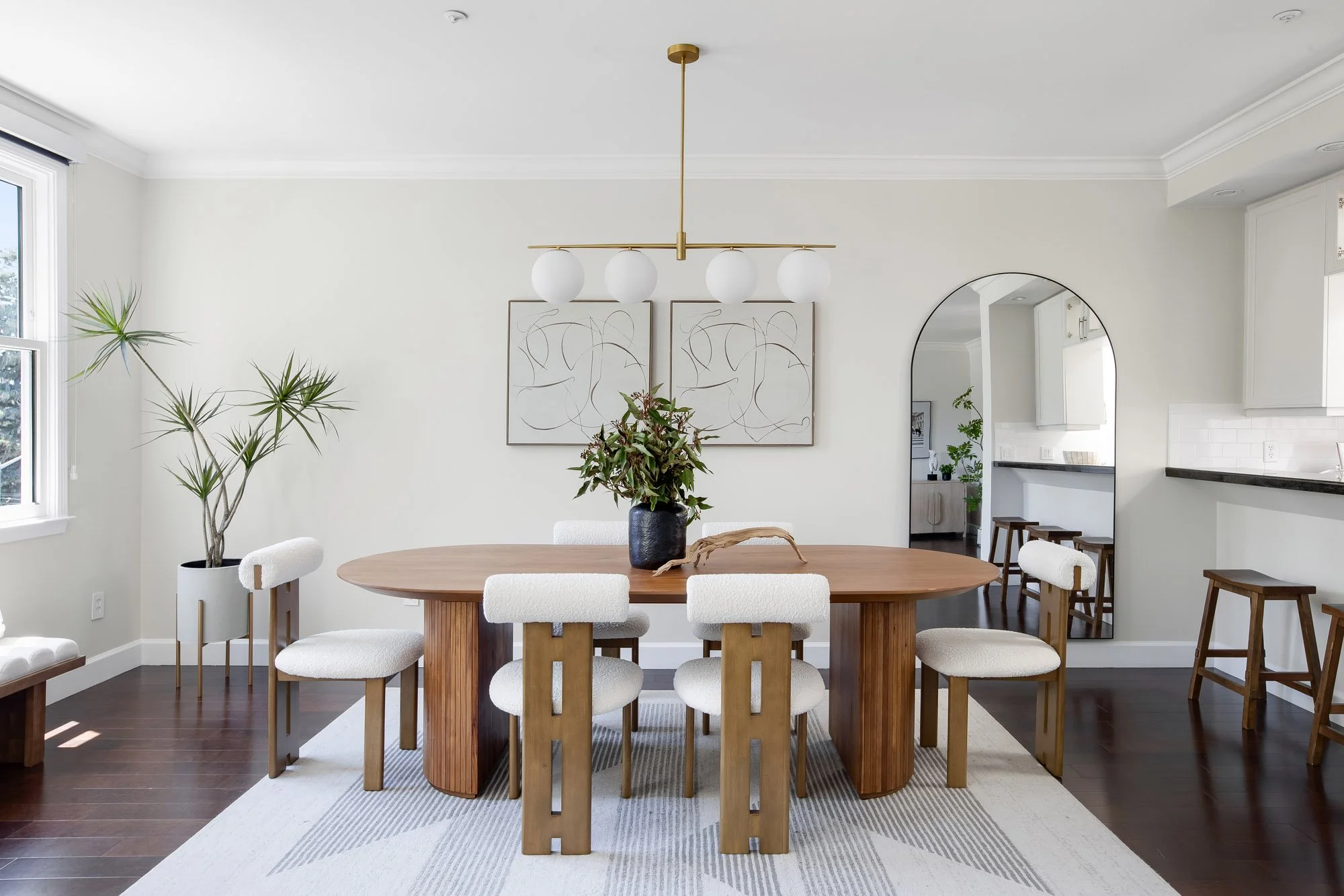 Elegant dining room at 2172 Fell Street San Francisco with oval walnut table, sculptural boucle chairs, brass globe pendant light, abstract diptych wall art, and arched floor mirror