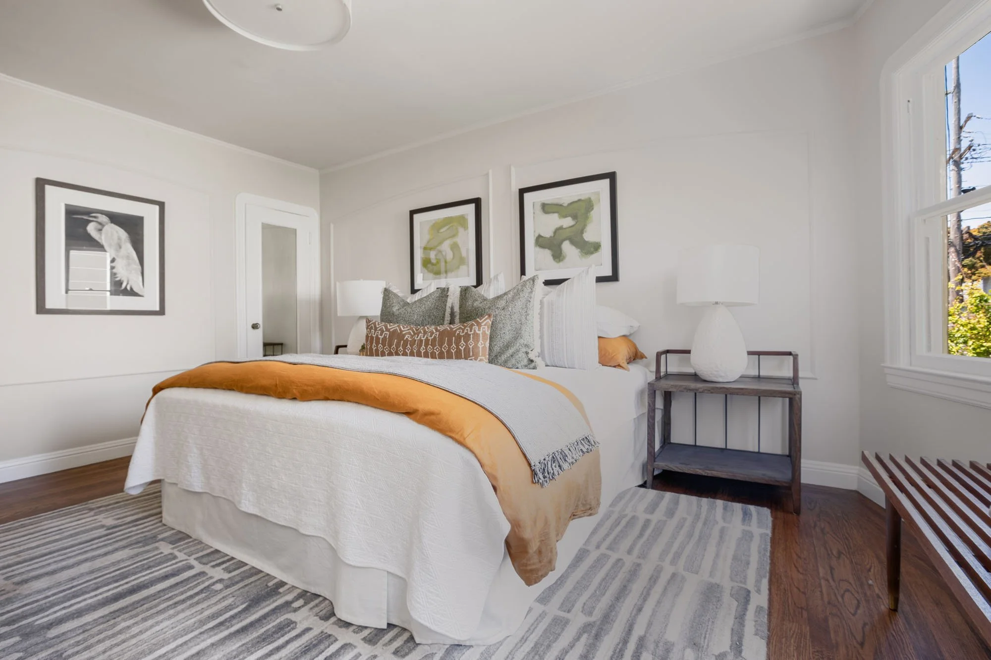 Staged bedroom at 2872 25th St featuring original wood floors, contemporary artwork, and a neutral color palette with ochre accents.
