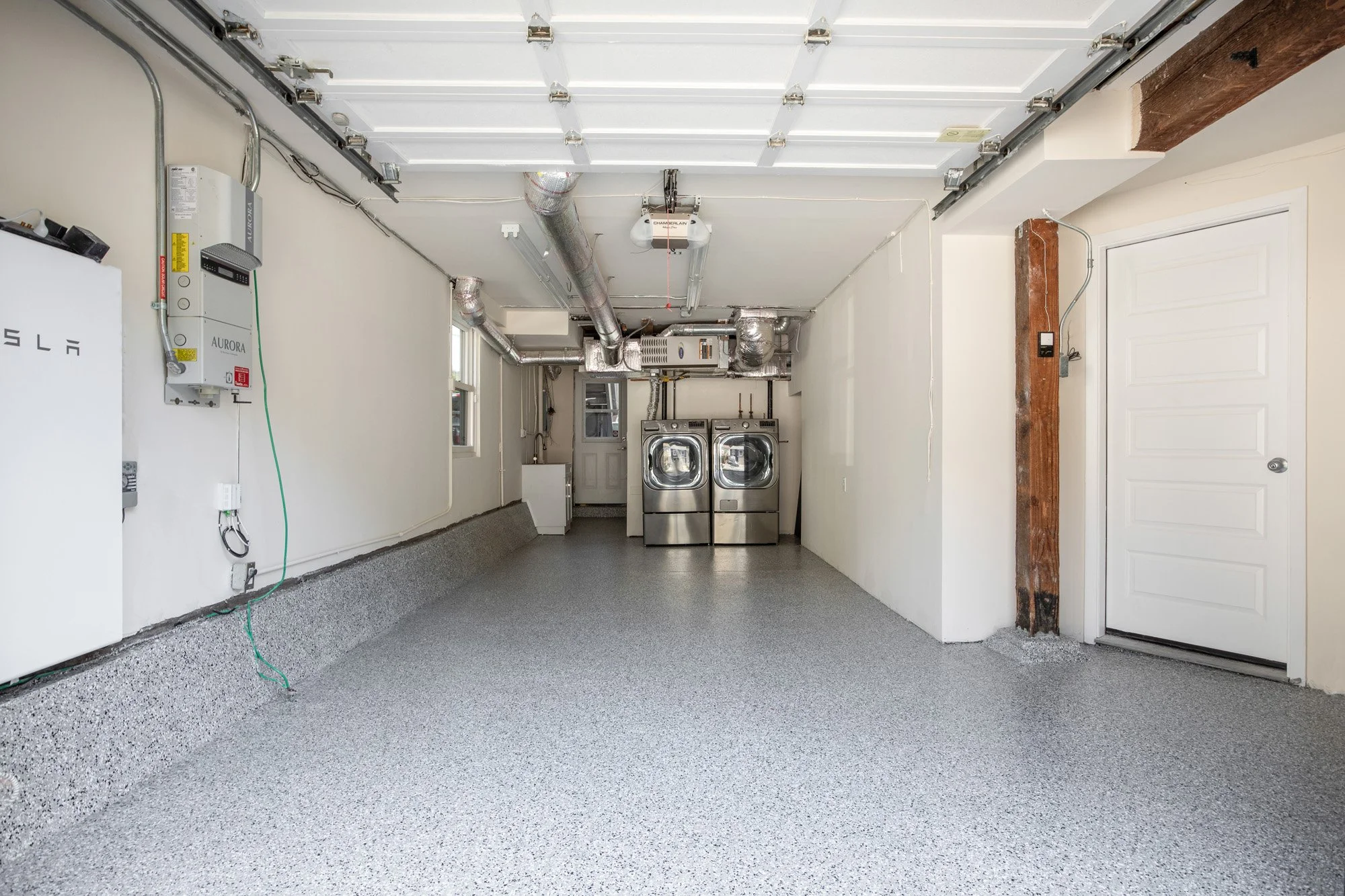 Finished garage with epoxy flooring, modern front-loading laundry units, and a Tesla Powerwall home battery backup system.