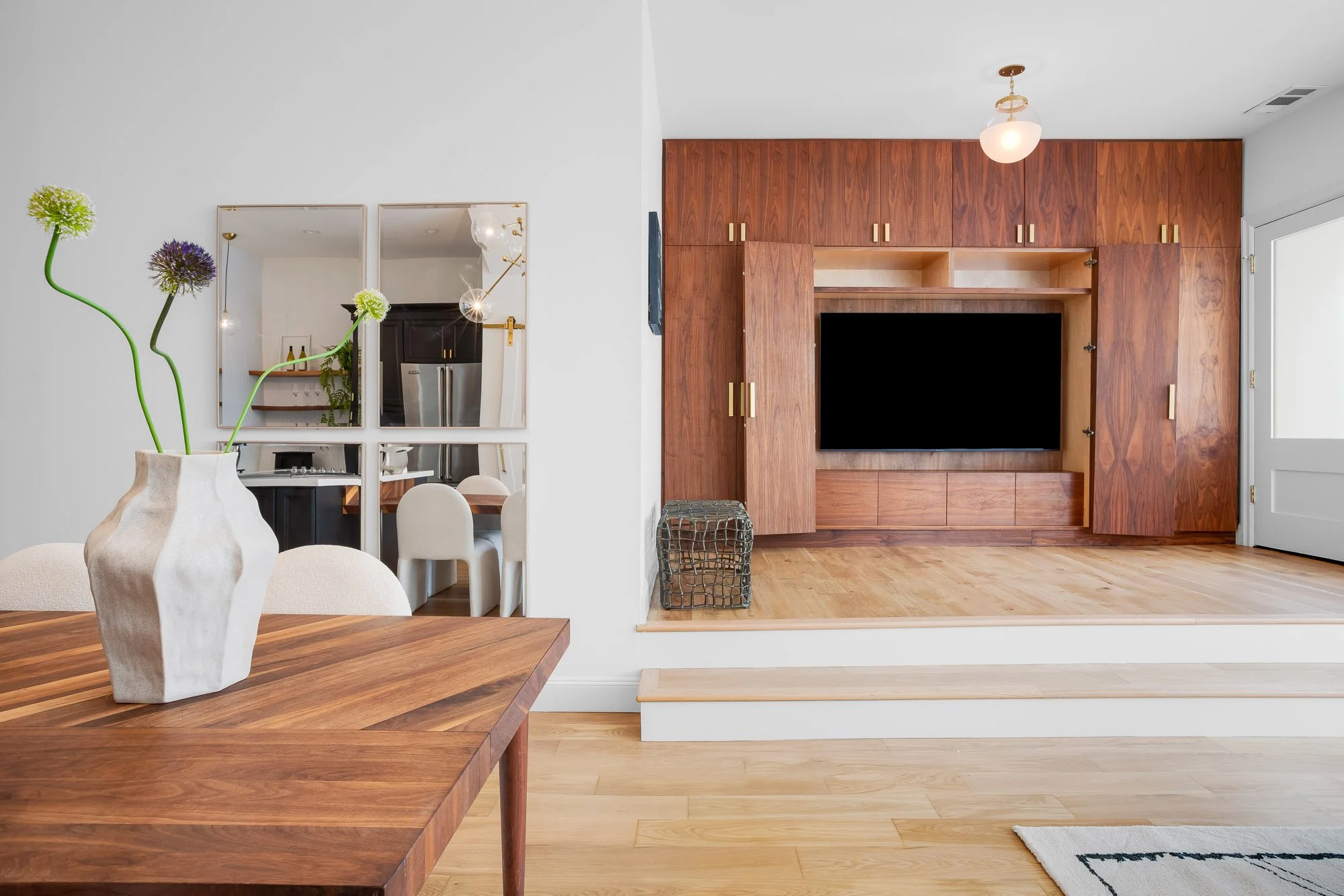 Custom walnut media wall with concealed flat-screen TV revealed behind cabinet doors, brass hardware accents, and raised white oak platform in Castro San Francisco luxury TIC at 4545 18th Street