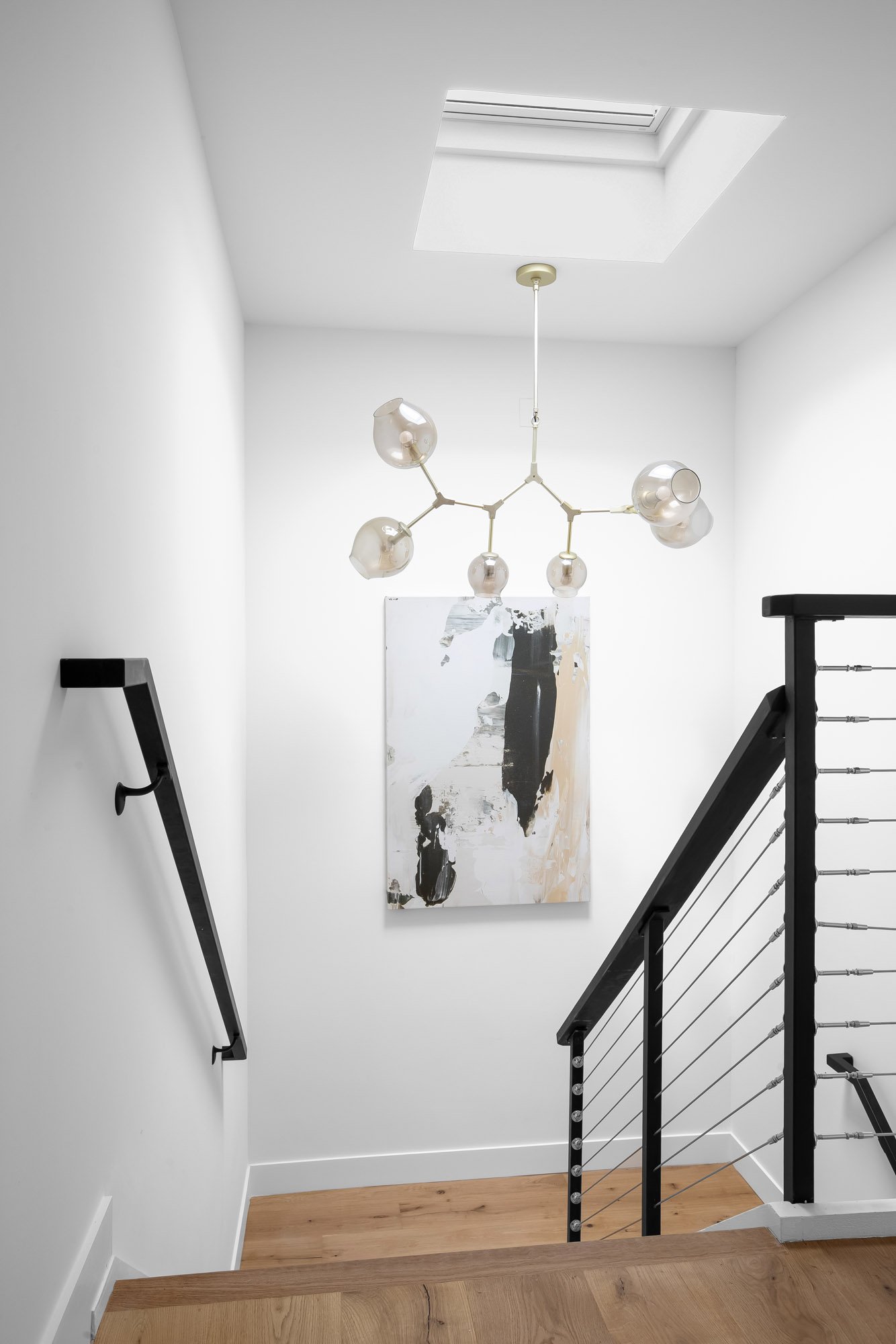 Stairwell at 75 Aloha Avenue in Golden Gate Heights, San Francisco, lit by a skylight above, with a black cable railing and oak treads.