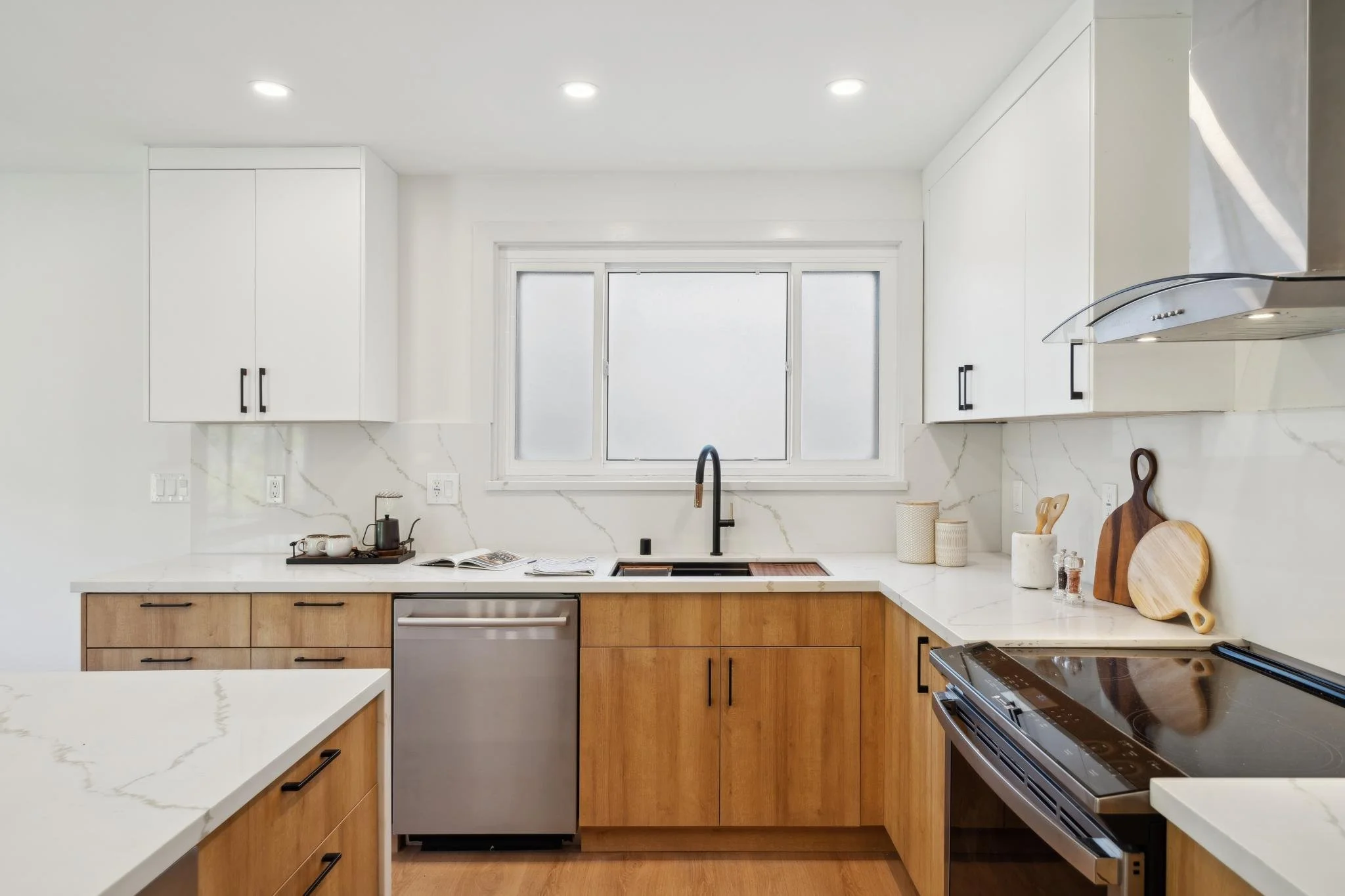 Detailed view of a modern kitchen workspace with a black gooseneck faucet, farmhouse sink, marble counters, and a professional stainless steel range.