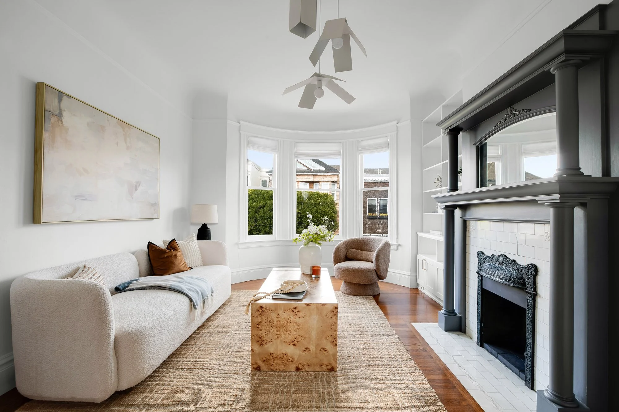Gracious Victorian living room with original curved bay windows, ornate wood-burning fireplace with cast iron surround, hardwood floors, crown molding, and built-in shelving in luxury Presidio Heights flat, San Francisco 