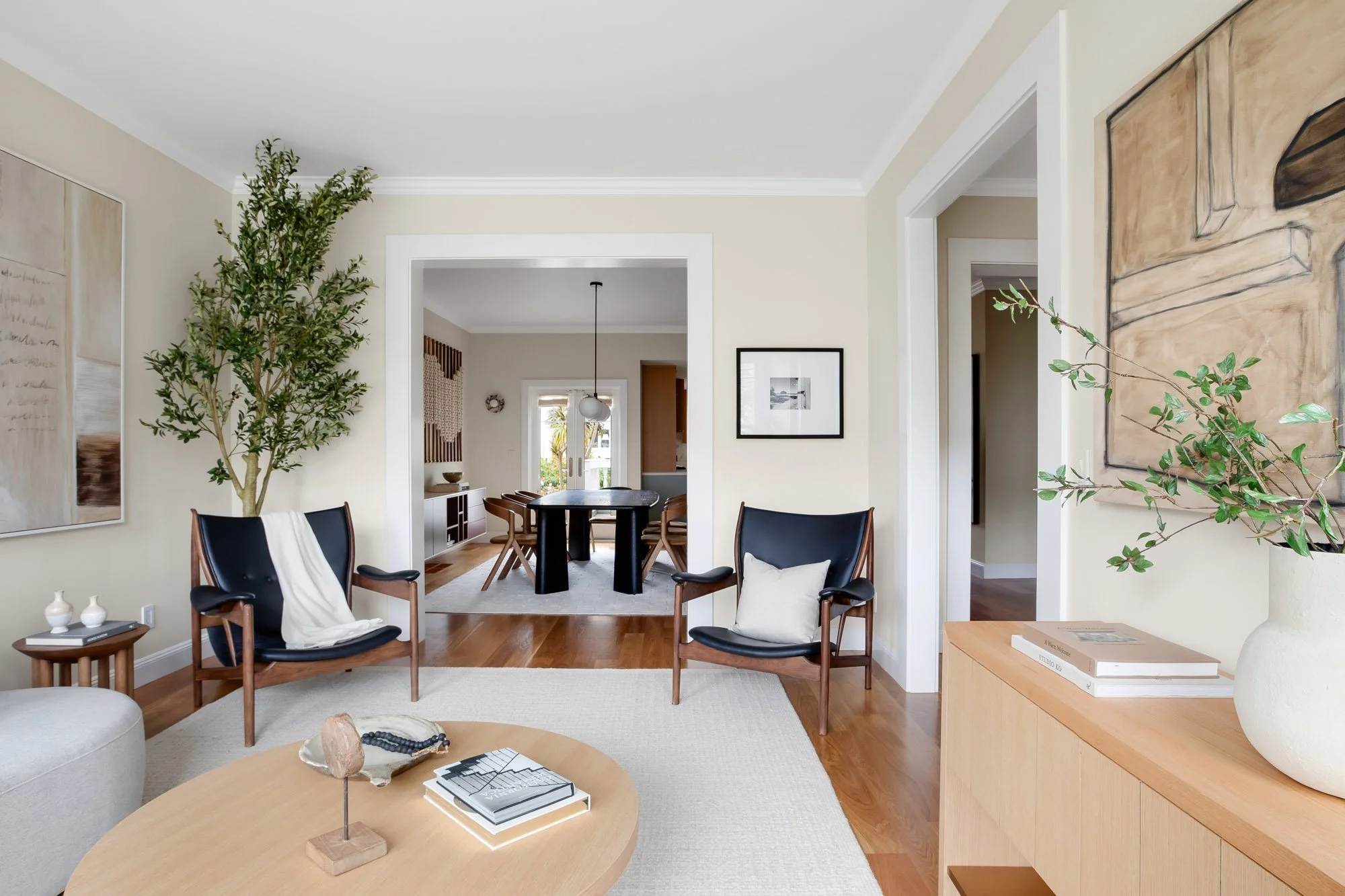 Front sitting room at 771 Elizabeth Street in Noe Valley, framed by twin black leather lounge chairs and a wide cased opening to the dining room beyond, with oak floors and gallery-style art.