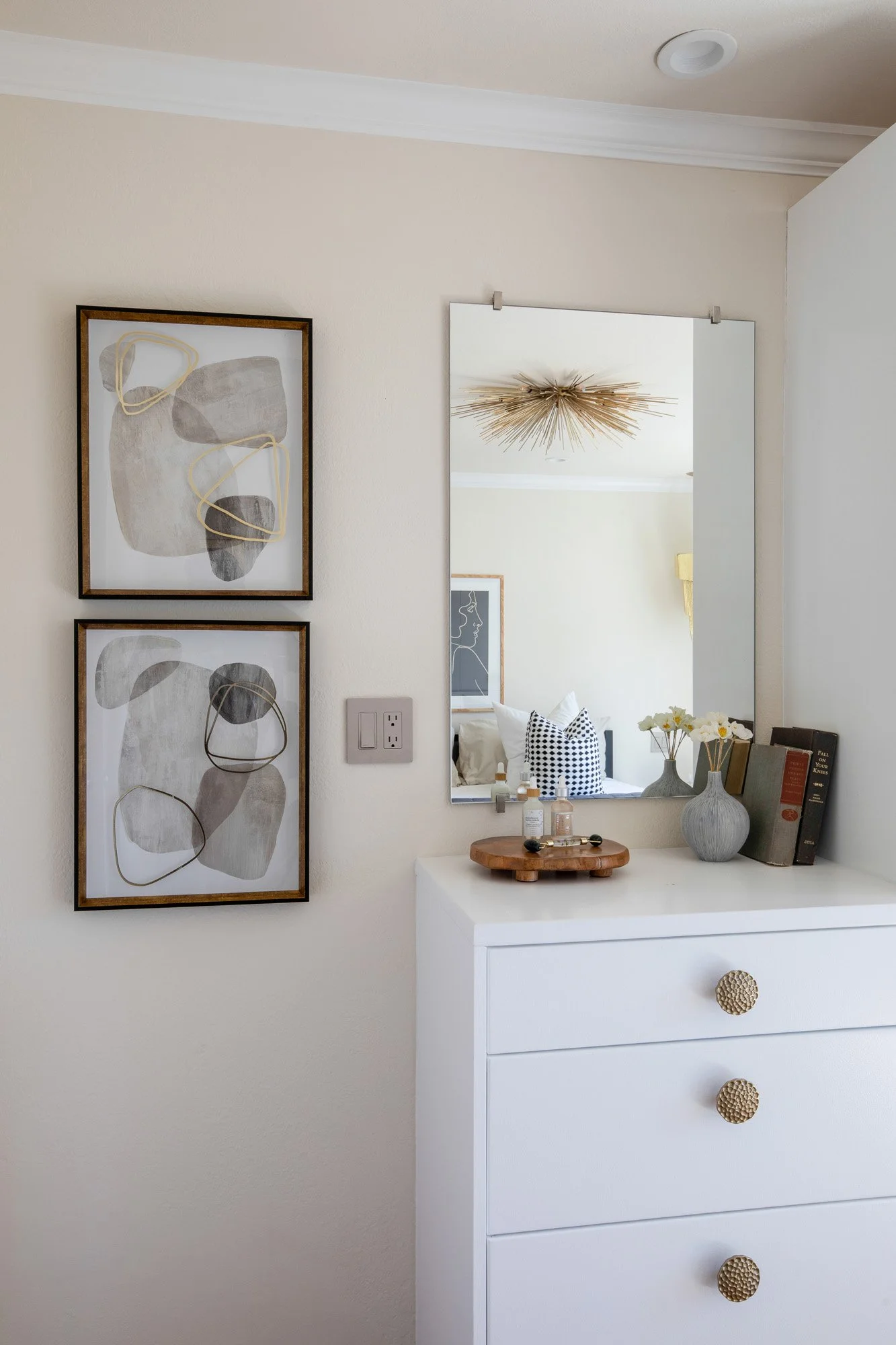 Detail of a modern bedroom dresser with gold sunburst light fixture and minimalist abstract wall art.