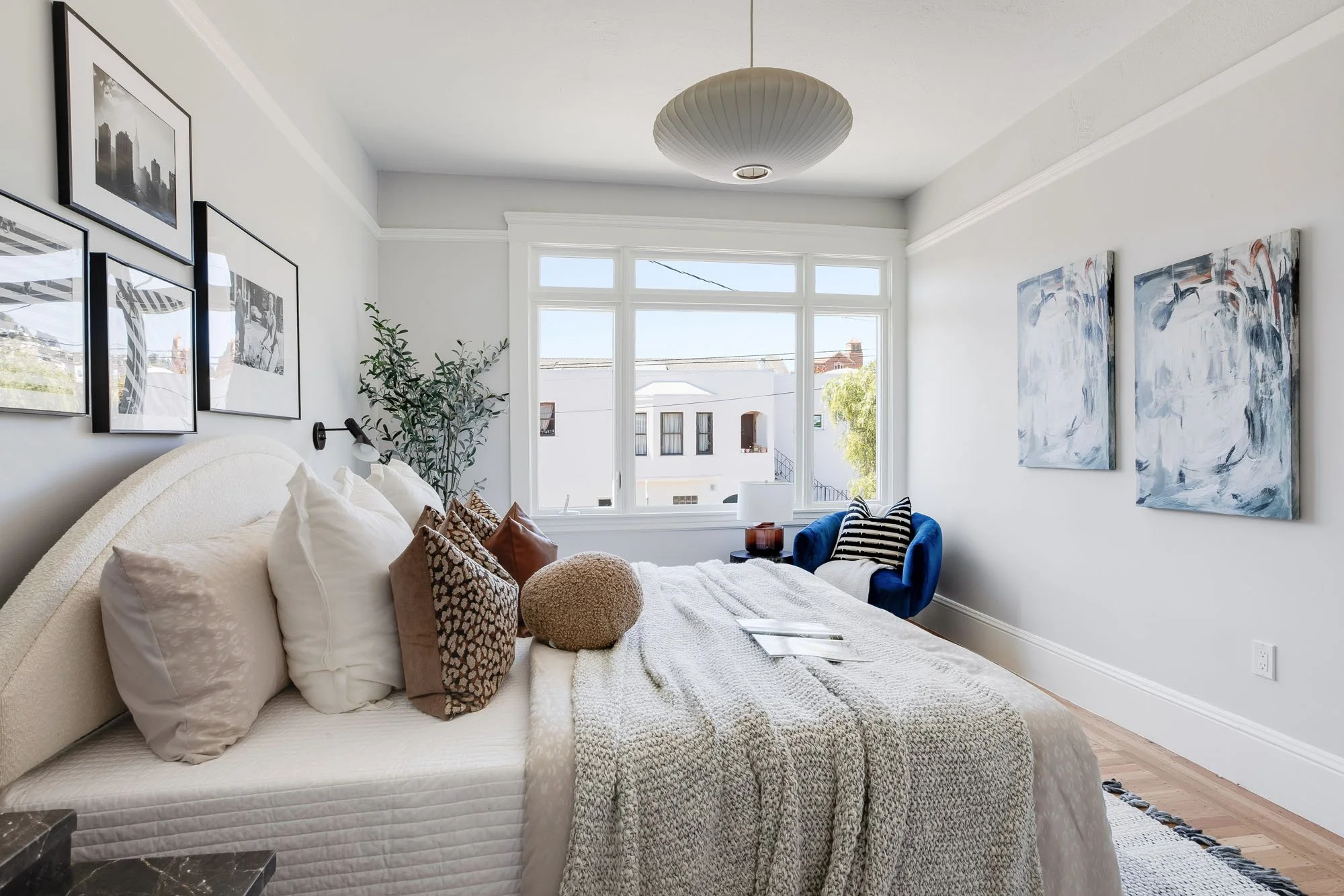 A different angle of the bedroom highlighting a deep blue velvet swivel chair, abstract blue wall art, and a modern pleated pendant light.