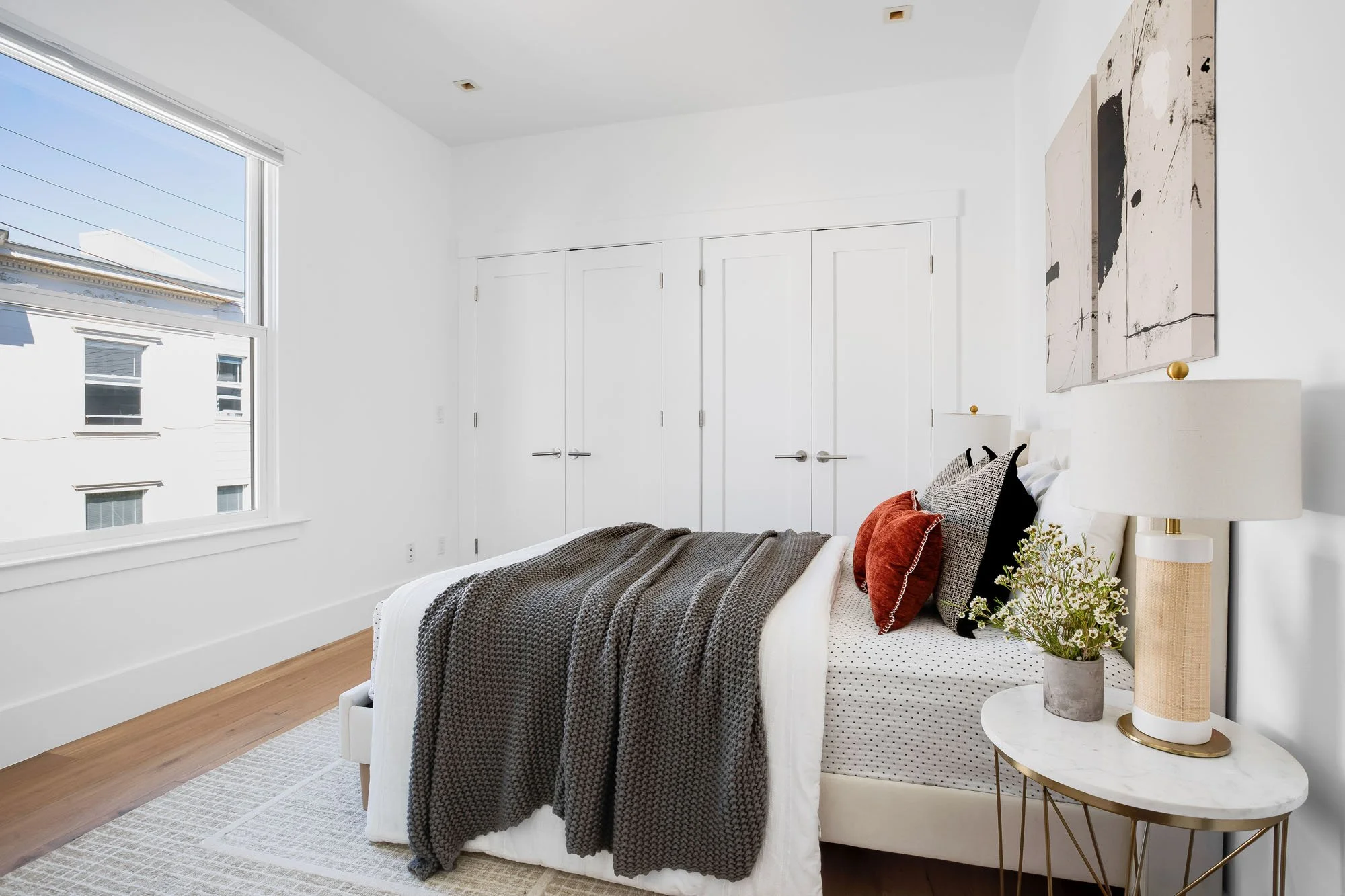 Bright bedroom in a luxury San Francisco condo featuring built-in white closets, hardwood floors, and modern layered bedding.