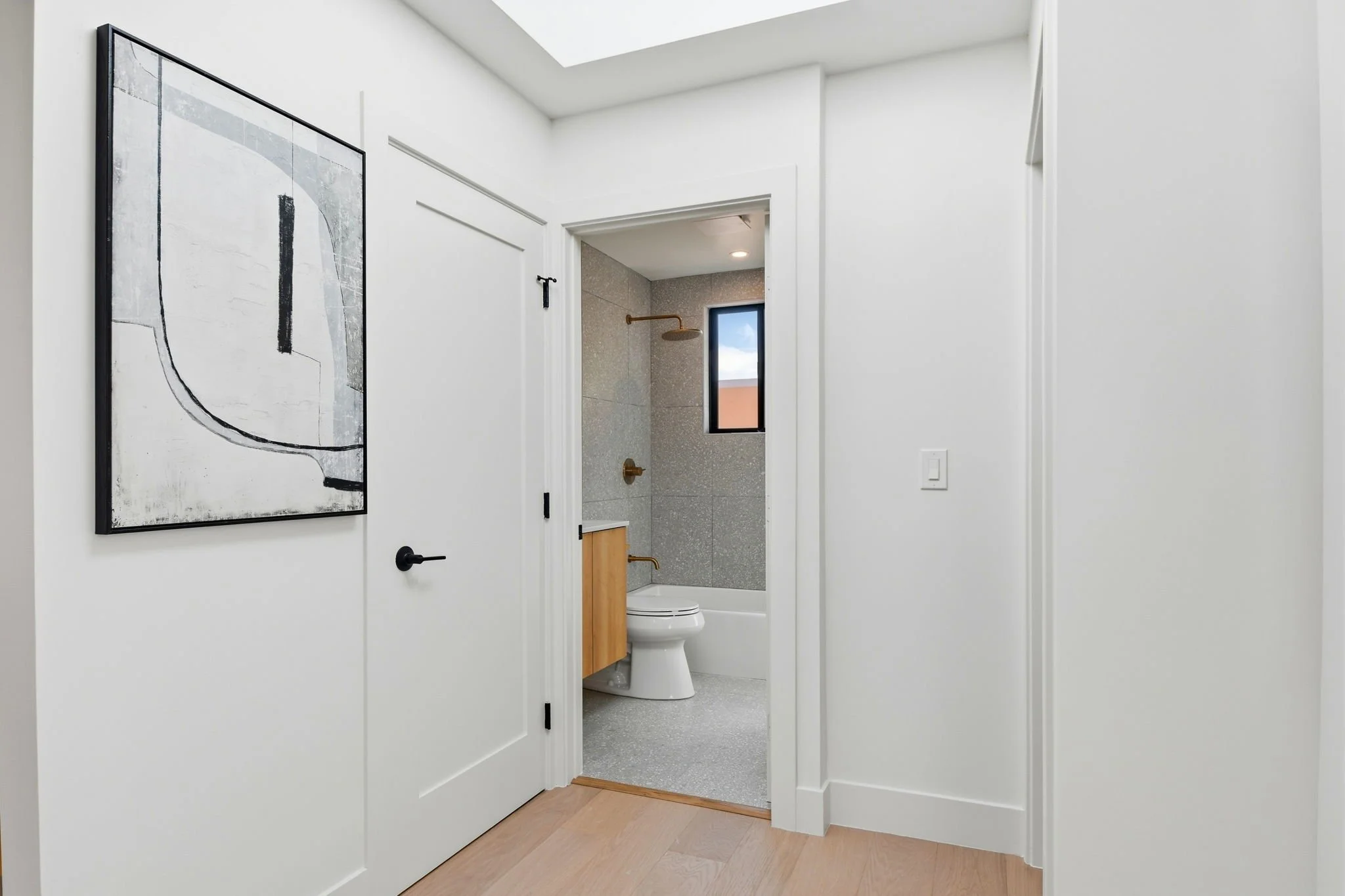Interior view of a luxury San Francisco home showing white shaker doors with matte black hardware leading to a gray stone-tiled bathroom.
