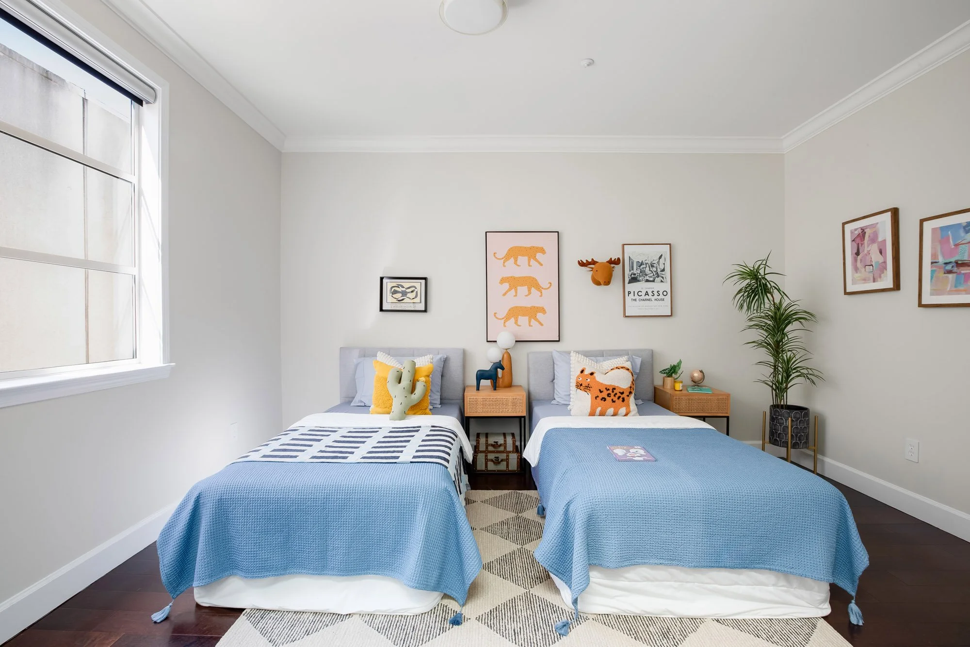 Third bedroom/Flexible use room at 2172 Fell Street San Francisco styled as a kids room with two twin beds, blue bedding, colorful wall art, rattan nightstands, and dark hardwood floors with geometric area rug.