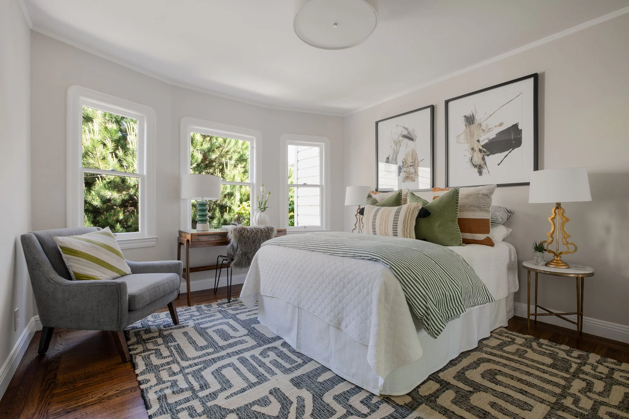 Primary bedroom with three large windows offering garden views, a patterned area rug, and contemporary artwork at 2872 25th Street.