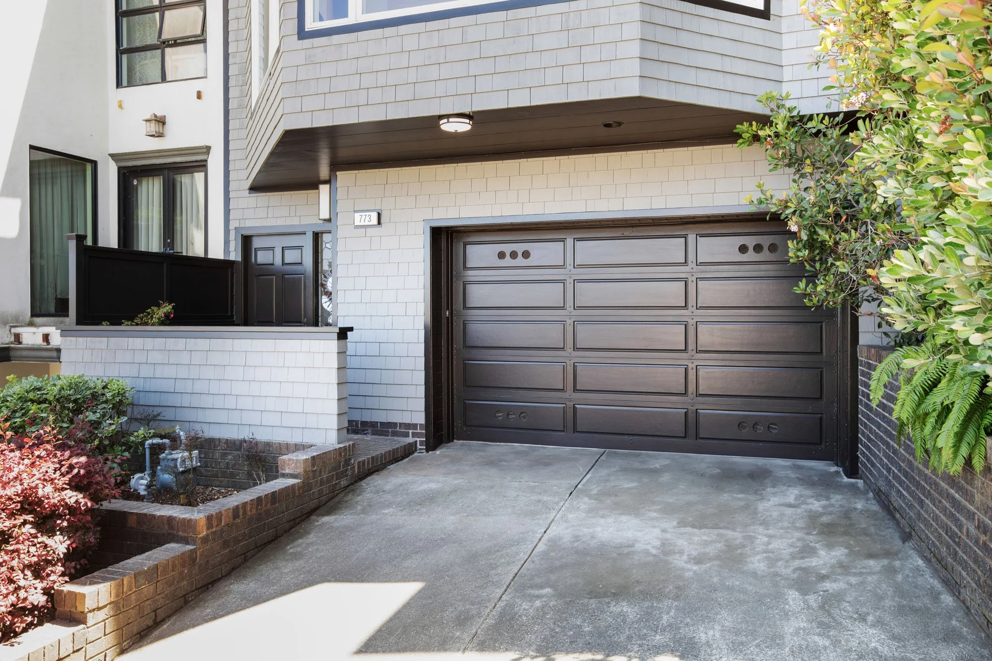 Curb appeal shot of a modern San Francisco residence on Duncan Street, featuring a dark wood-paneled garage door, grey shingle exterior, and professional landscaping.